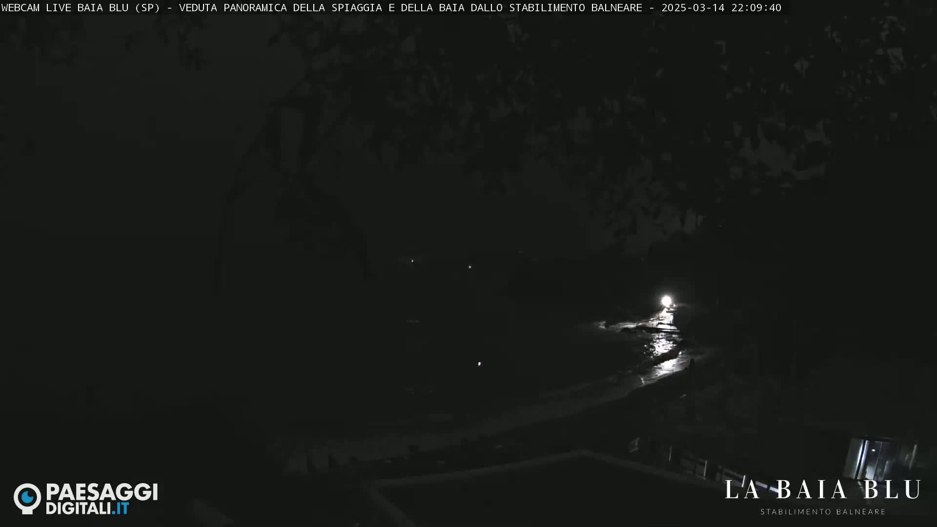 A dark, nighttime view of a beach and bay, illuminated by a single light source.