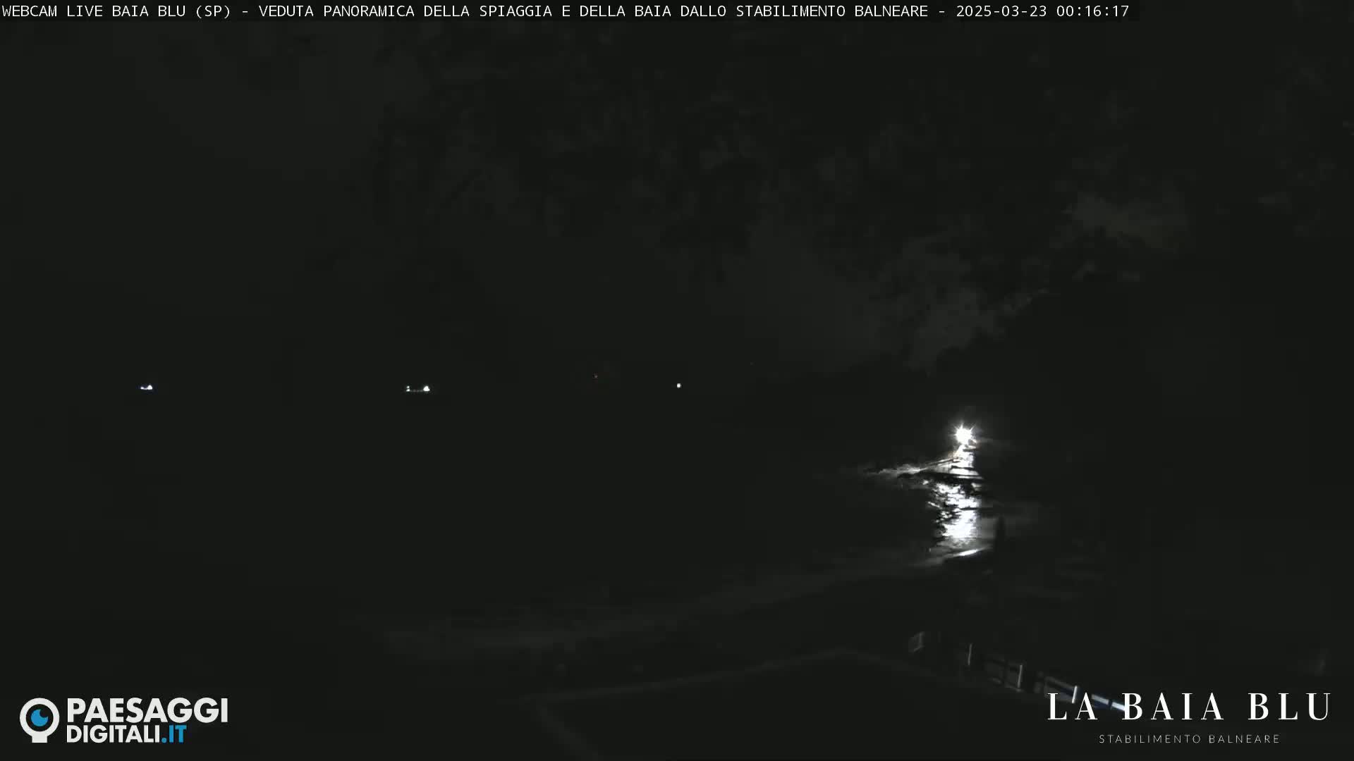 A nighttime, dark view of a beach with a single bright light reflecting on the water.