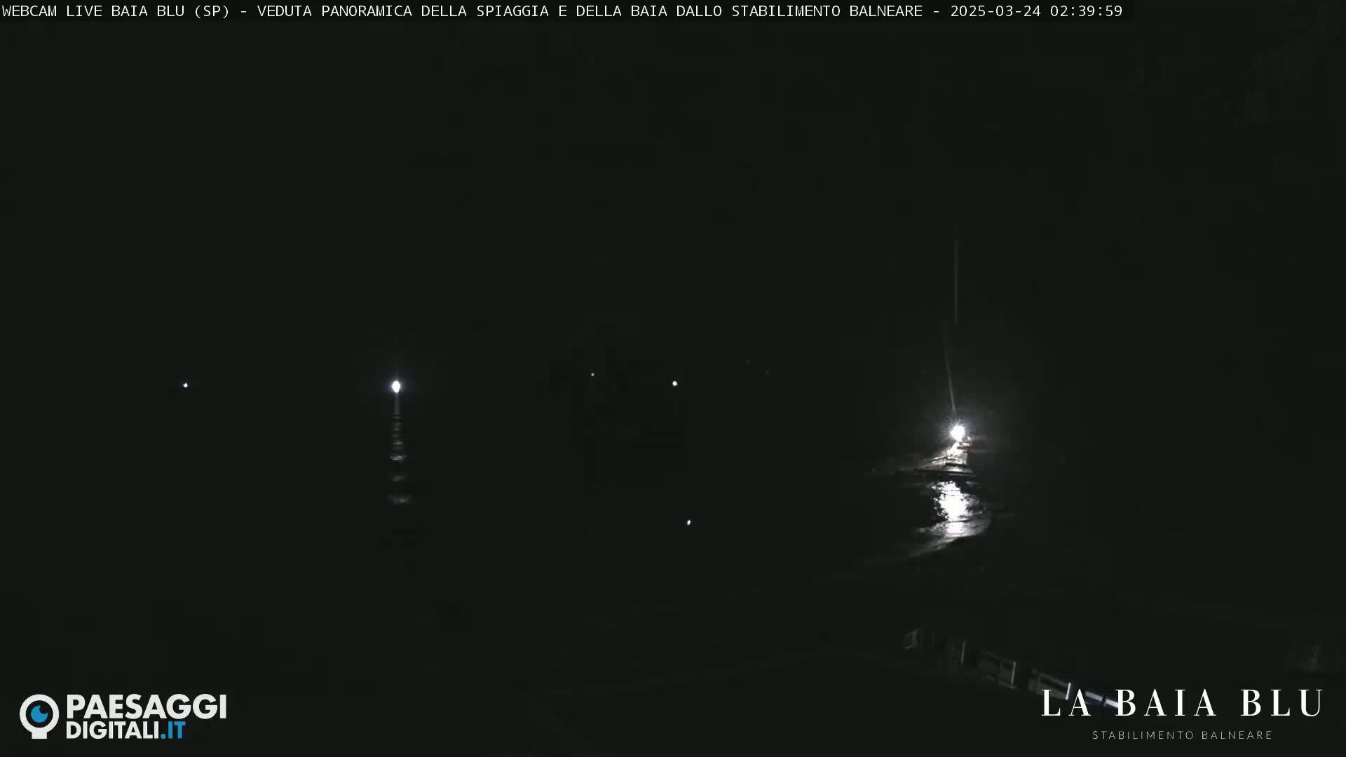 A dark nighttime scene shows a body of water reflecting a few distant lights.