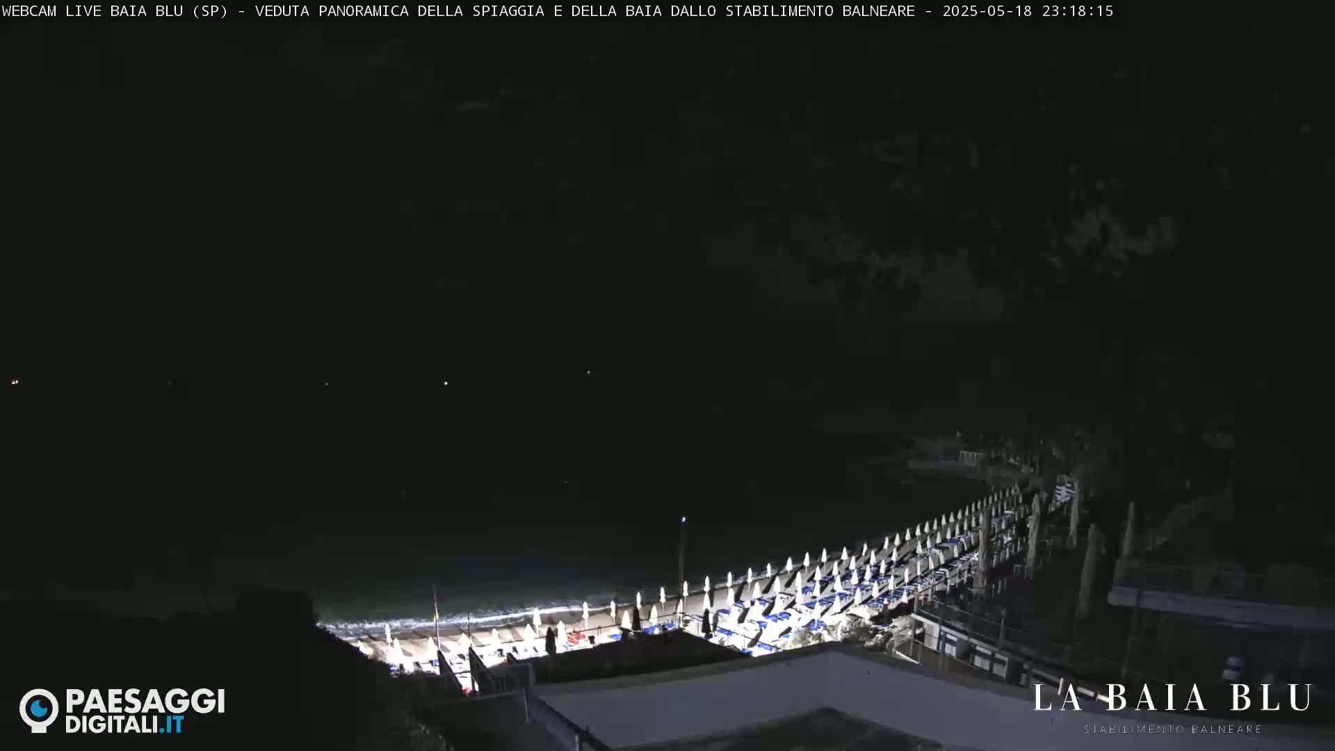 A nighttime, panoramic view of a beach with rows of closed beach umbrellas and chairs under a dark sky.