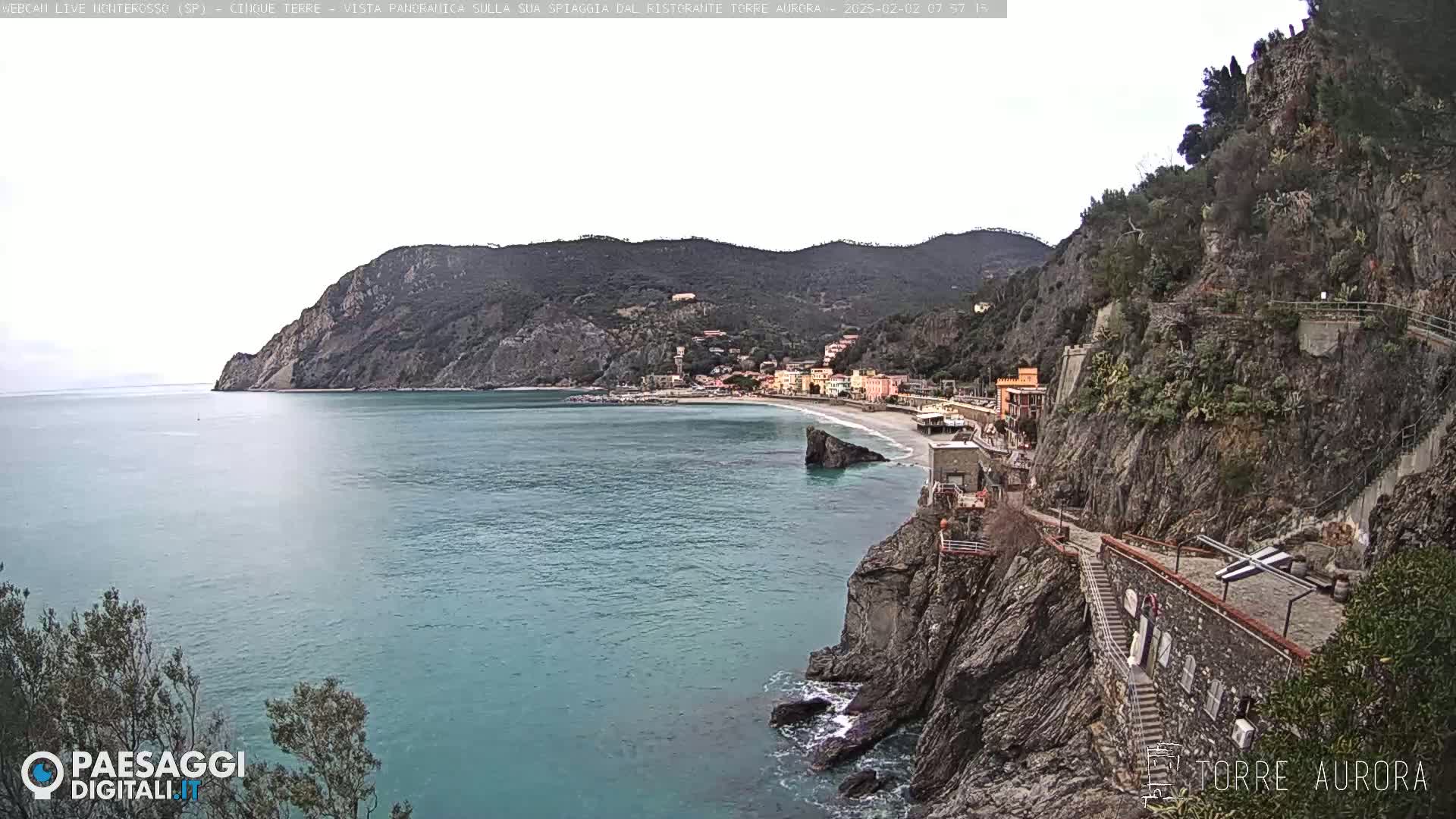 A coastal town nestled between steep cliffs and a calm, blue-green sea under an overcast sky.