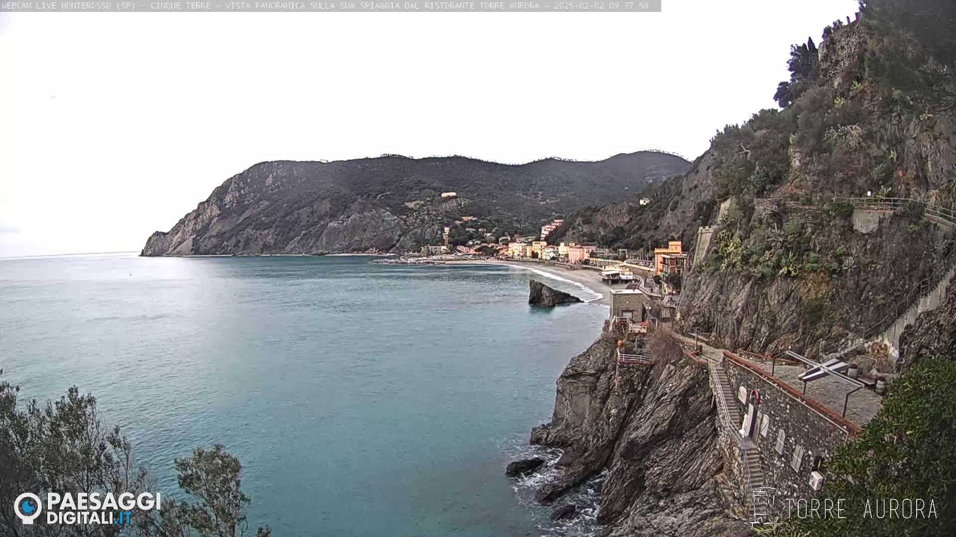 A coastal town nestled between steep cliffs and the sea, under a mostly cloudy sky.