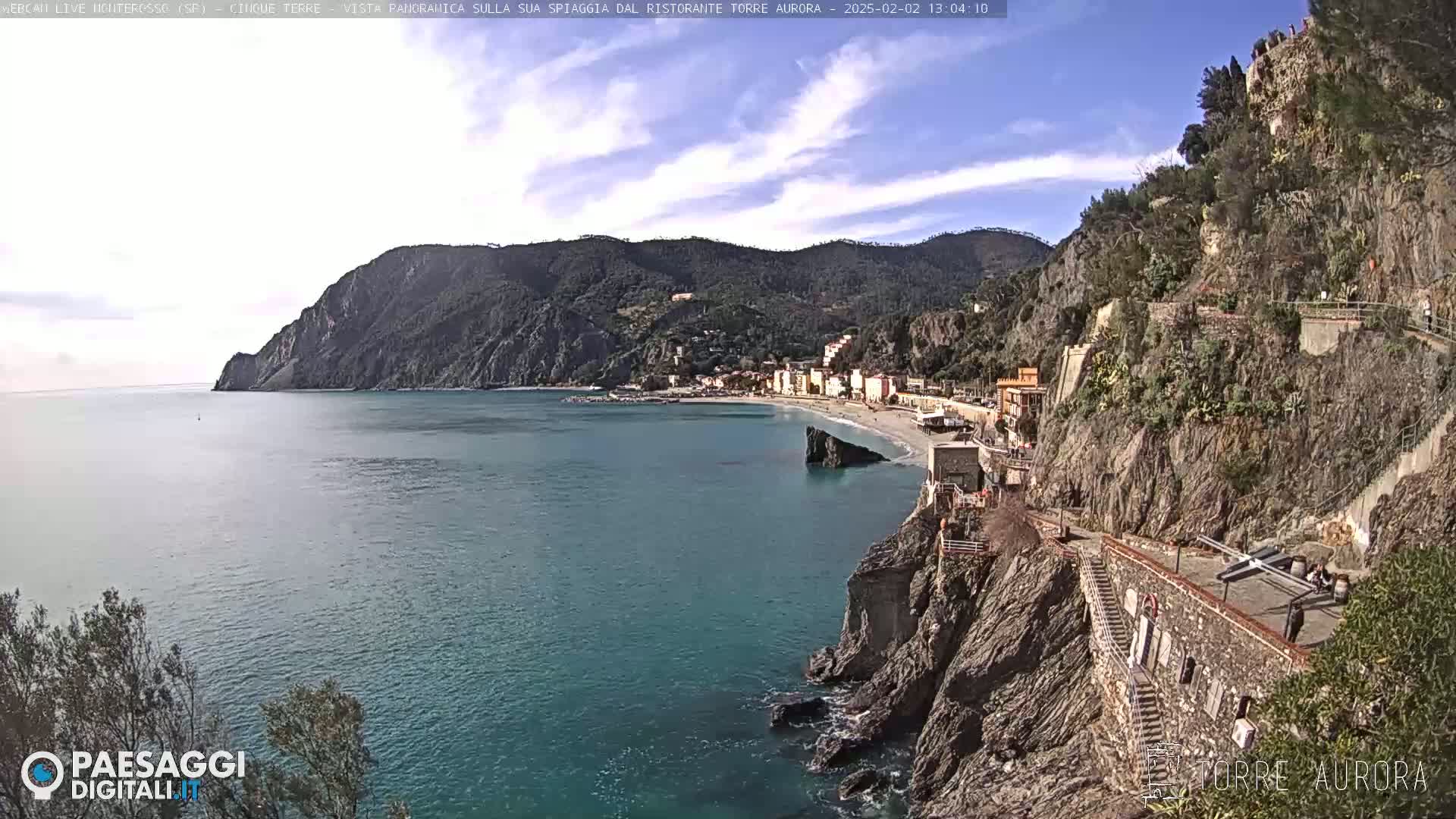 A coastal town nestled between steep, rocky cliffs and a calm, blue sea under a mostly clear sky.