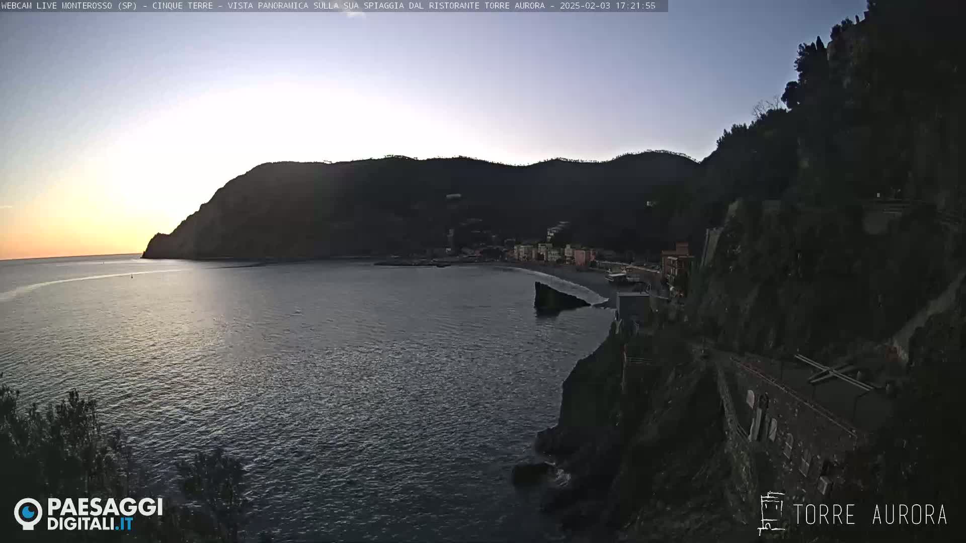 A coastal town nestled between dark hills, with a calm sea at twilight.