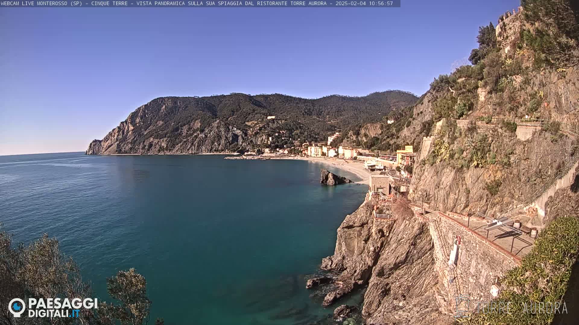 A coastal town nestled on a rocky cliff overlooking a calm turquoise sea under a clear blue sky.