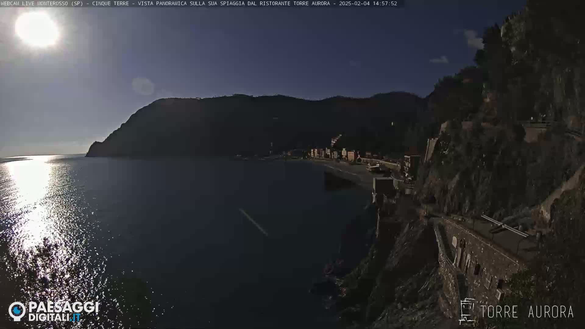A sunny day overlooking a calm body of water with a small town nestled against a cliffside.