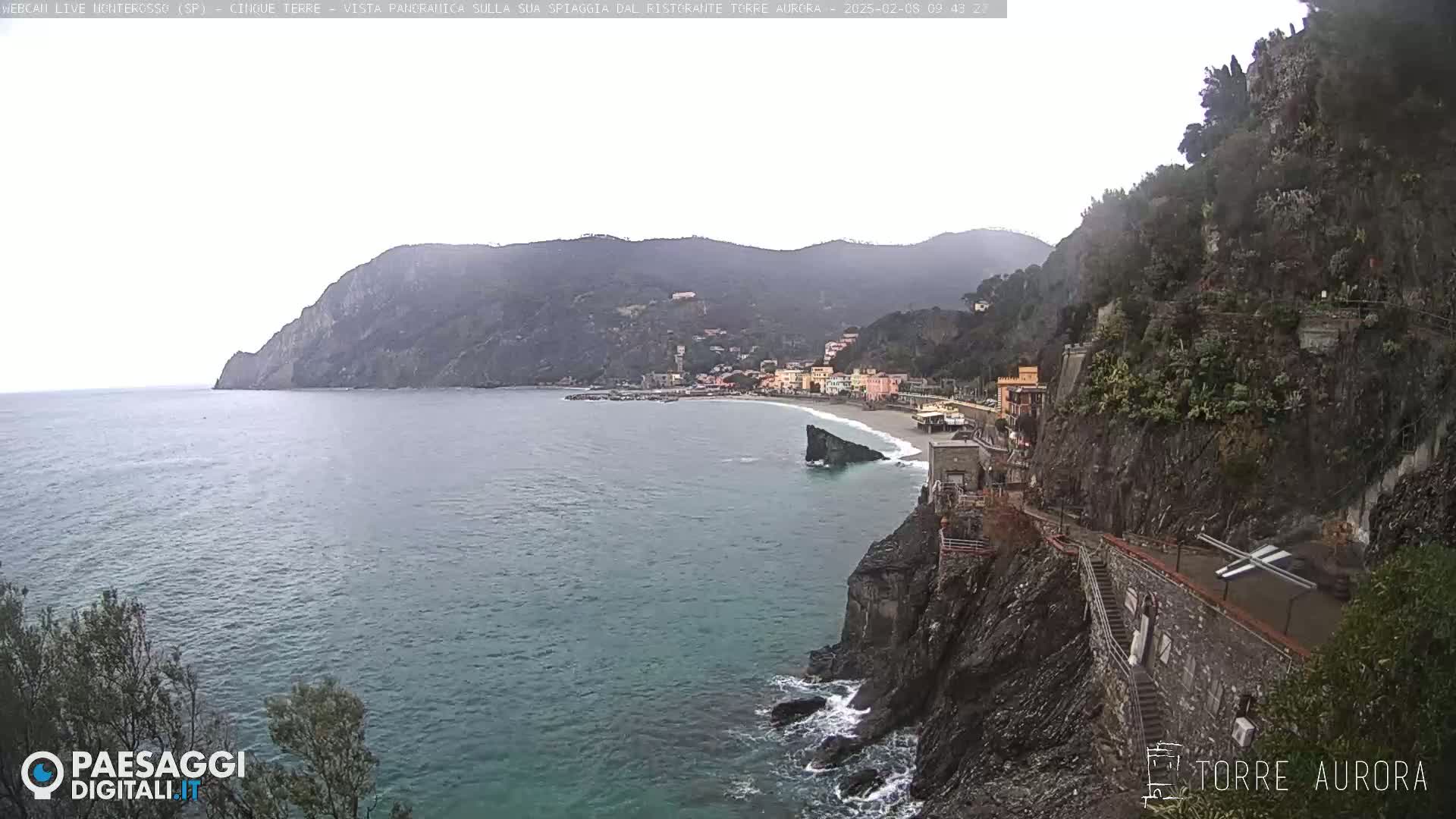 A coastal town nestled between steep cliffs and a calm, overcast sea.
