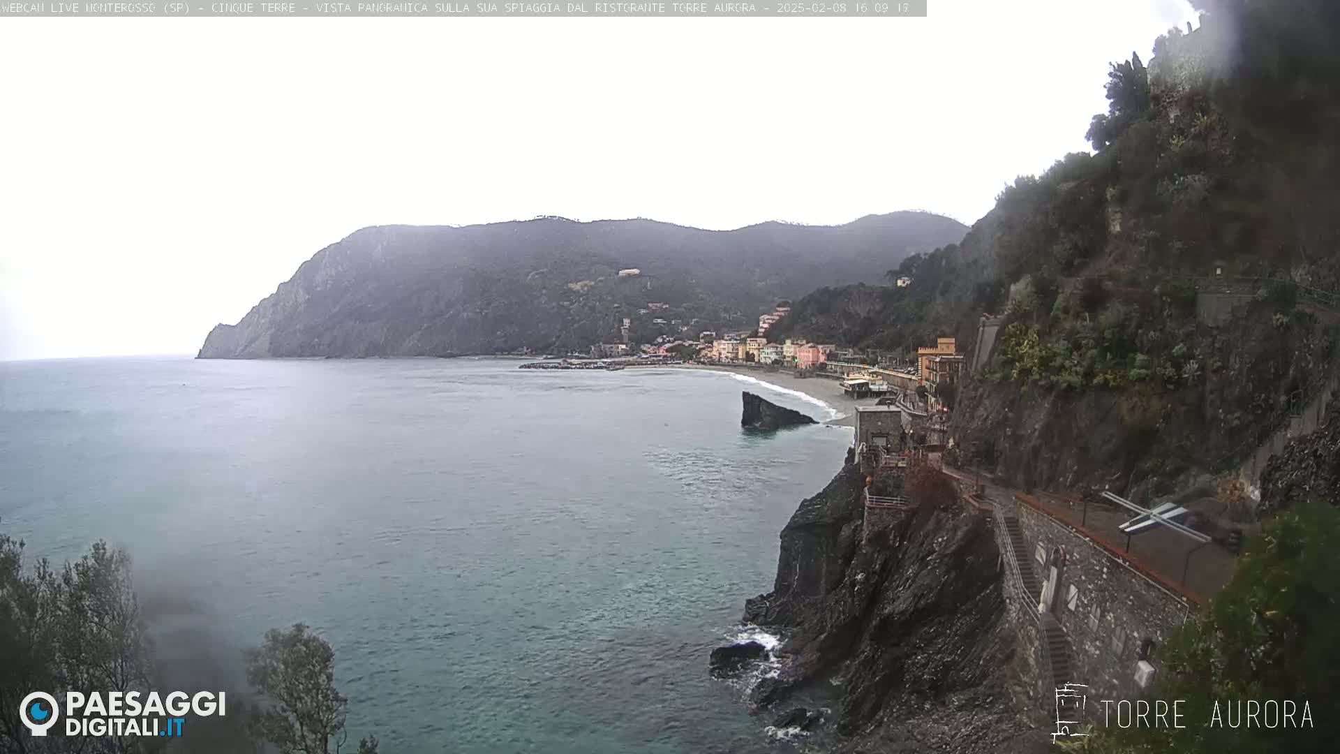 A coastal town nestled between steep cliffs and a calm, gray sea under an overcast sky.