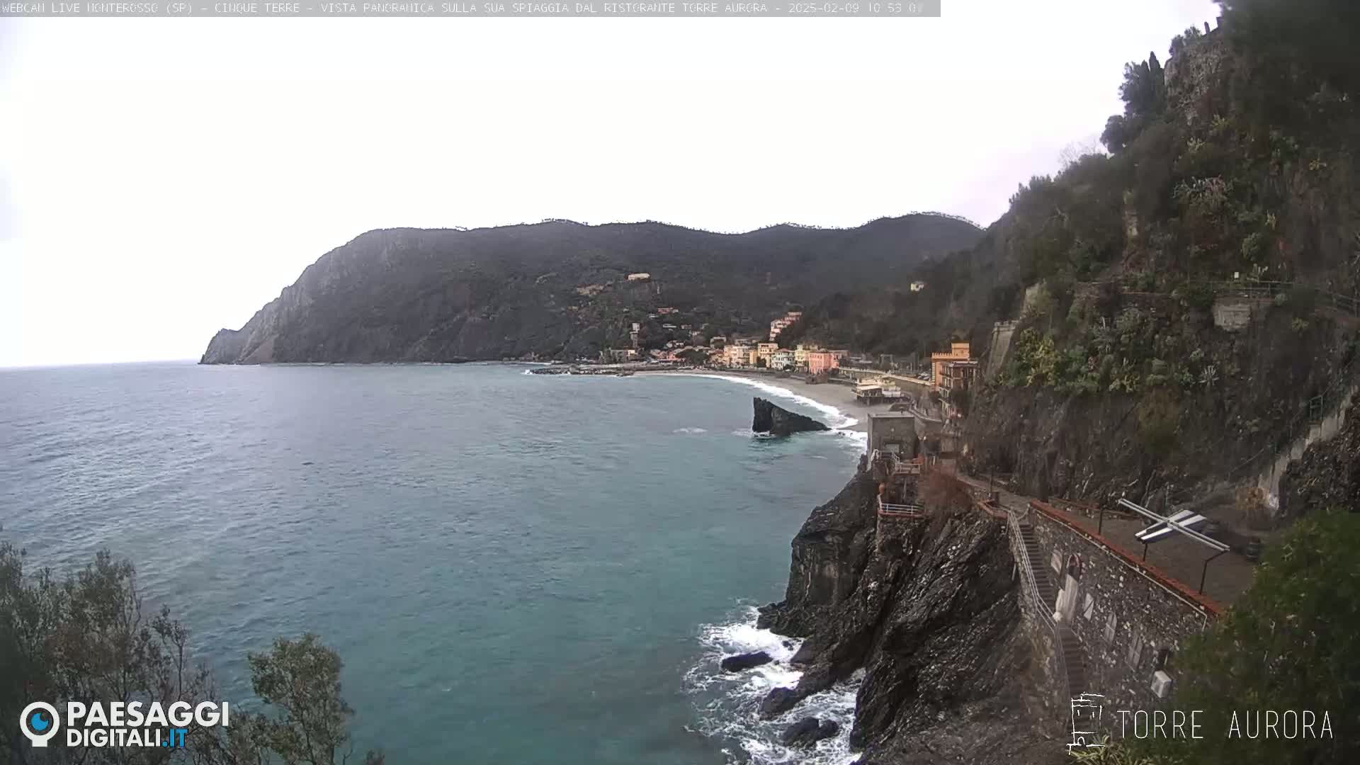 A coastal town nestled between steep cliffs and a calm sea under an overcast sky.