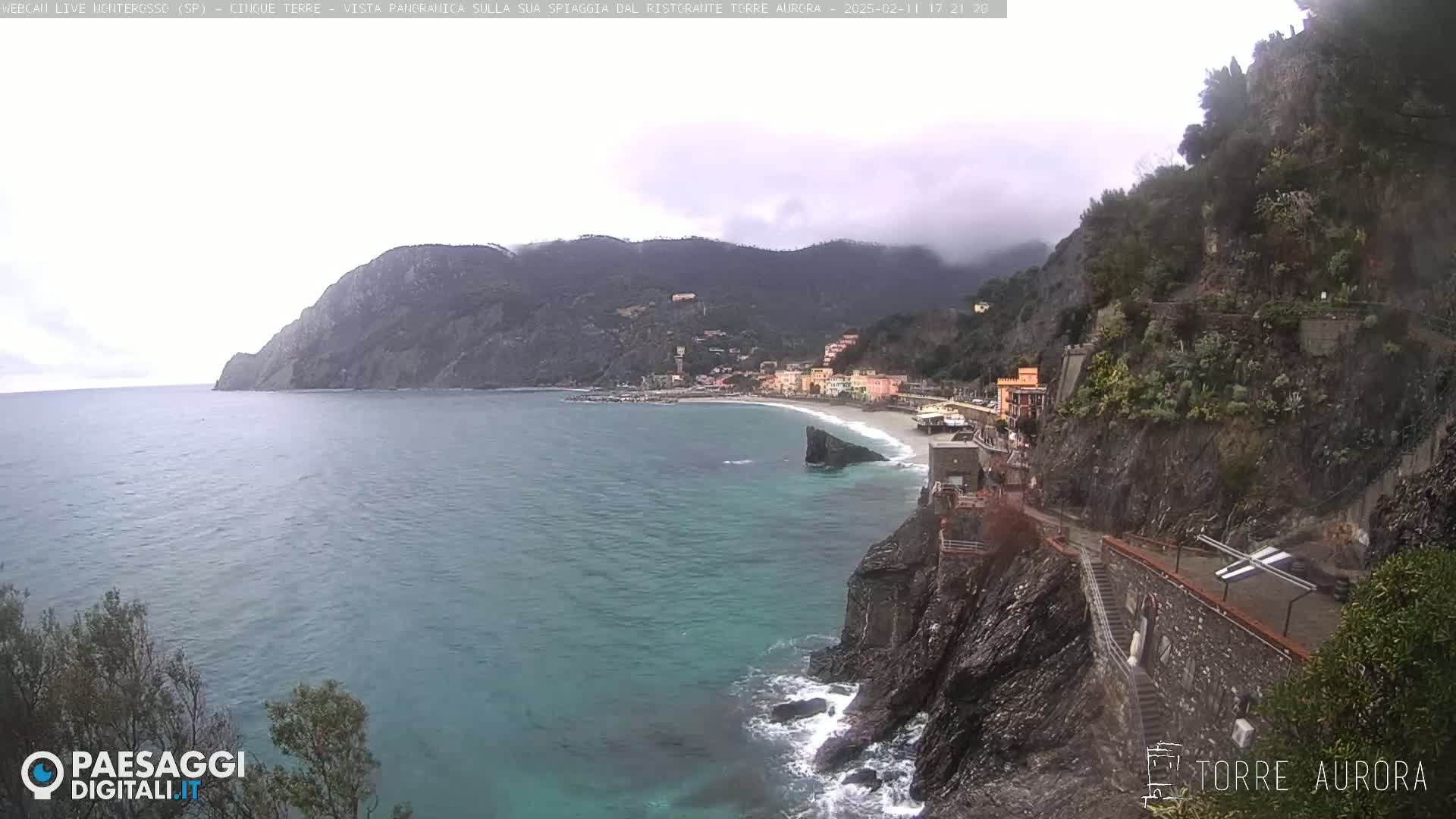 A coastal town nestled between steep, rocky cliffs, with a calm sea and overcast skies.