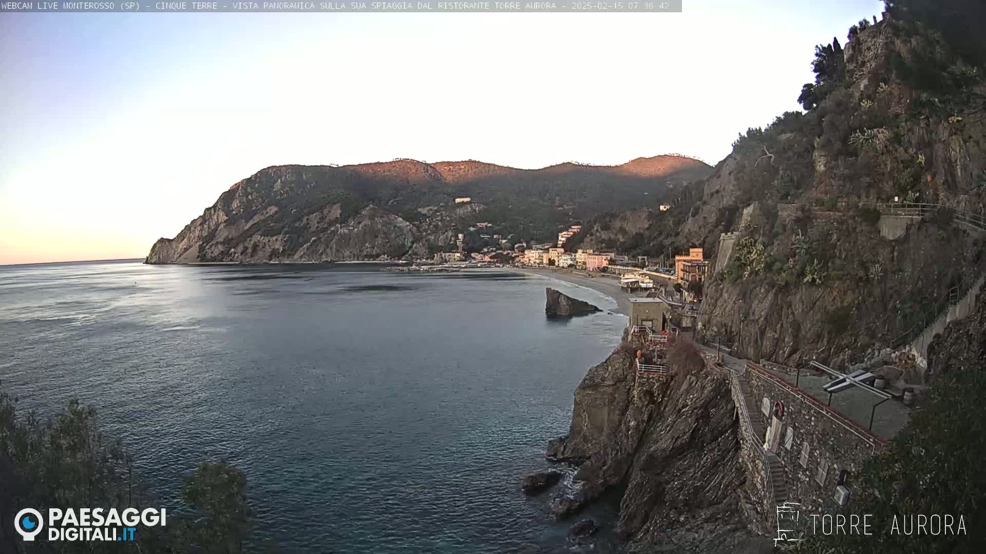 A coastal town nestled between steep cliffs and a calm sea is bathed in the soft light of dawn.