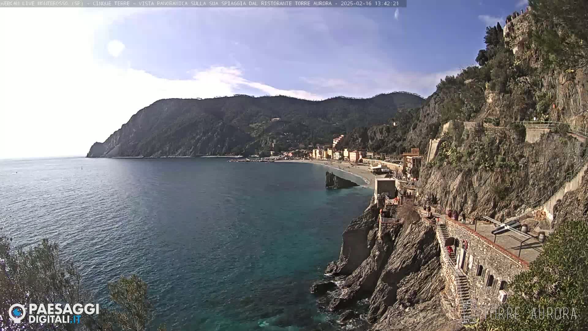 A coastal town nestled between steep cliffs and a calm blue sea under a mostly clear sky.