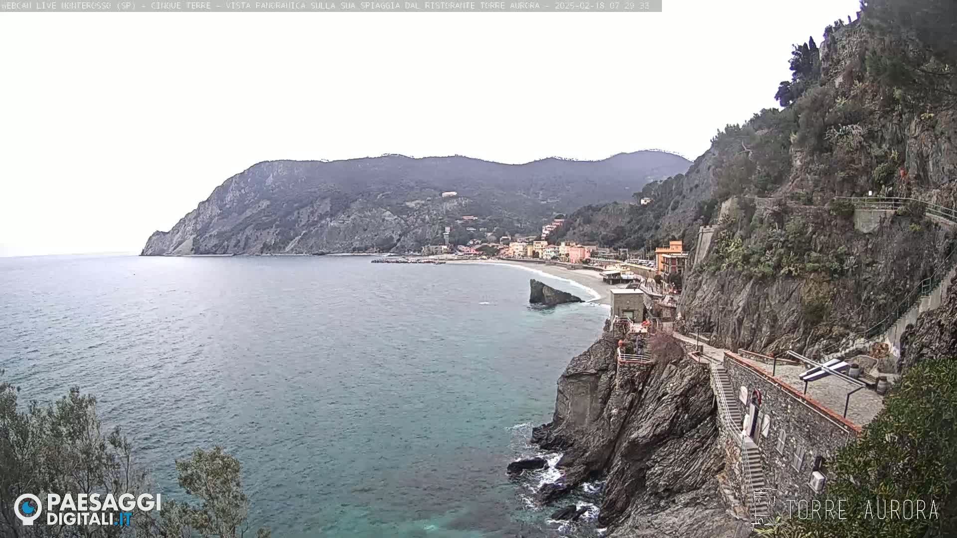 A coastal town nestled between rocky cliffs and a calm sea under an overcast sky.