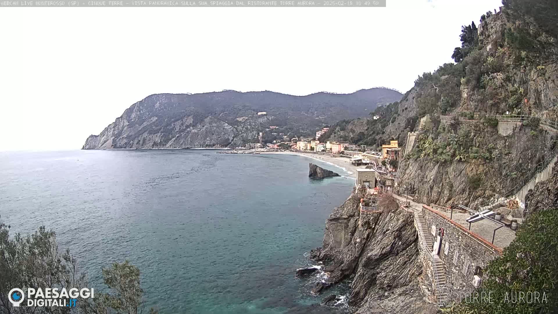 A coastal town nestled between rocky cliffs and the sea, under a mostly cloudy sky.