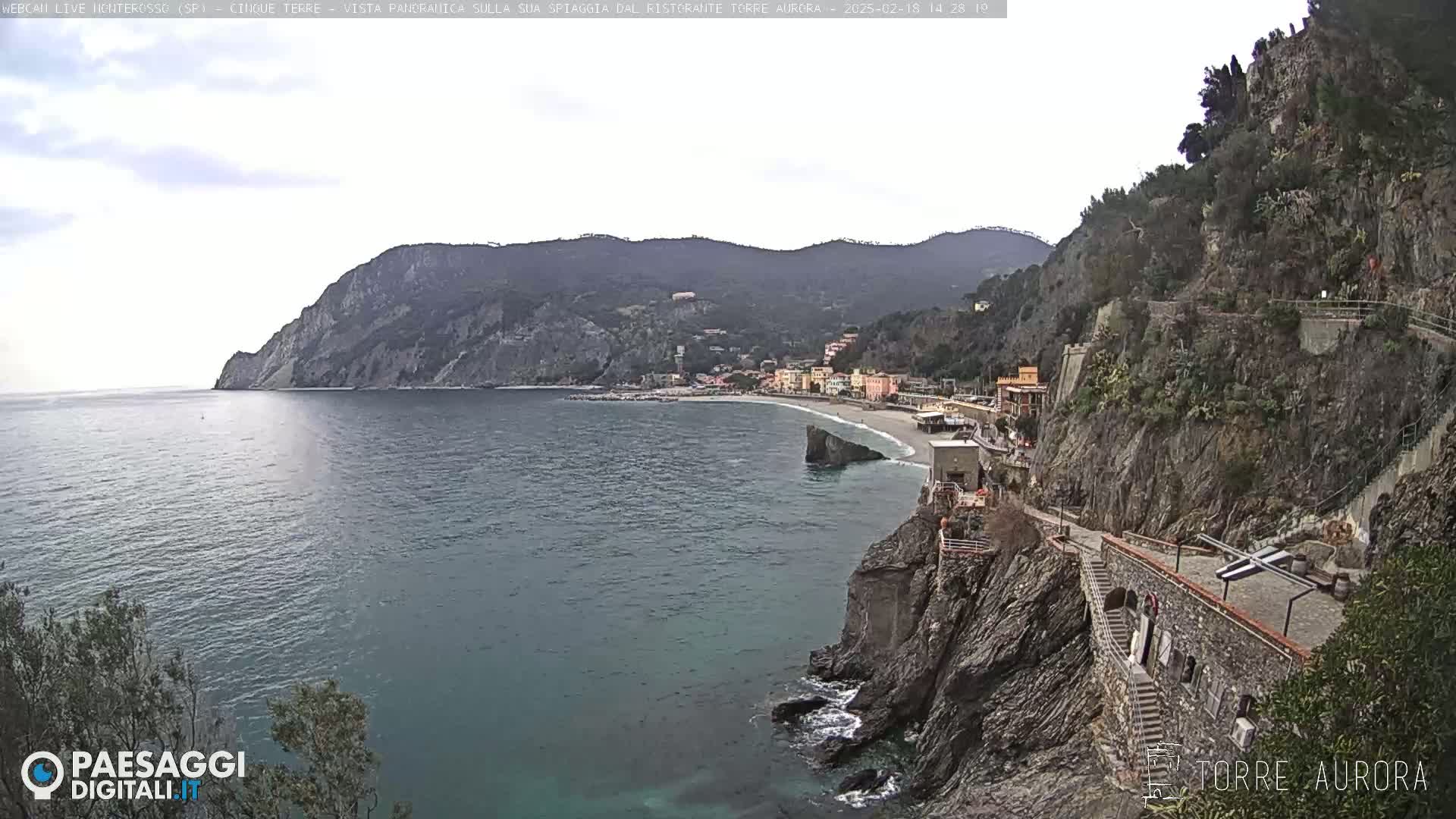 A coastal town nestled between steep cliffs and a calm sea under an overcast sky.