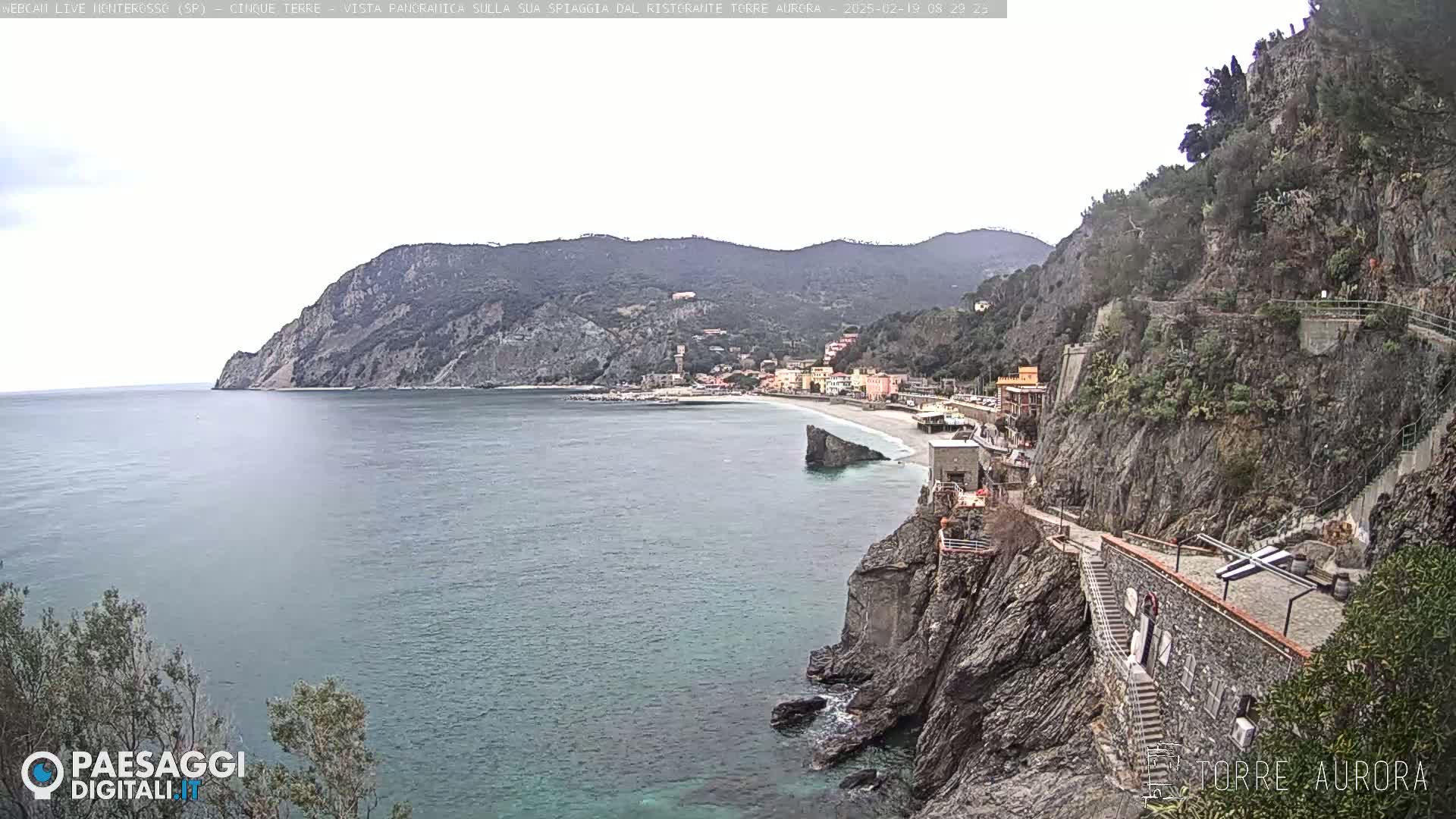 A coastal town nestled between steep, rocky cliffs and a calm sea under an overcast sky.