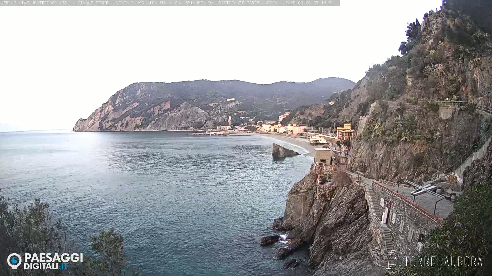 A coastal town nestled between steep cliffs and a calm sea under a mostly cloudy sky.