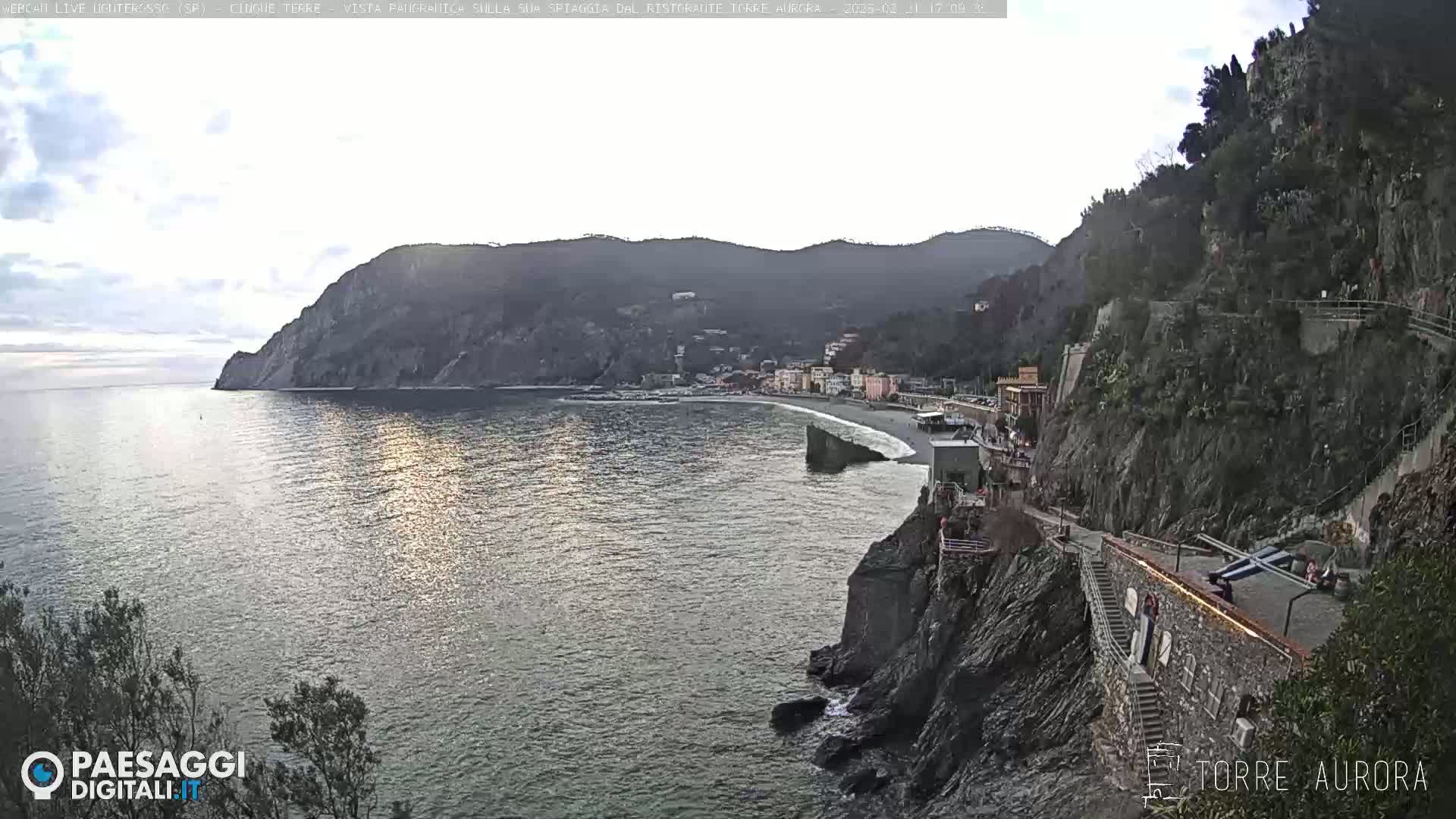 A coastal town nestled between steep cliffs and the sea under a mostly cloudy sky.