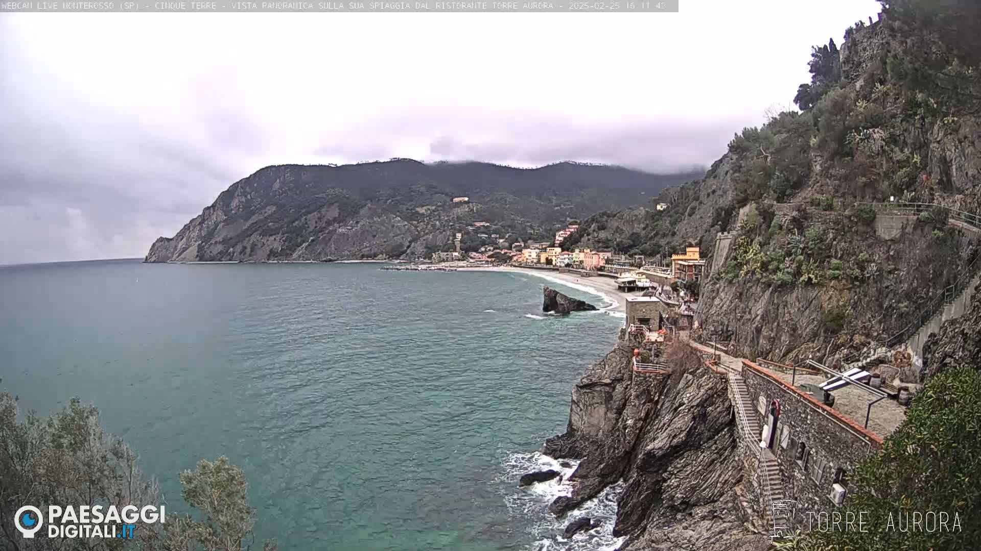 A coastal town nestled between steep cliffs and a calm, greenish-blue sea under an overcast sky.