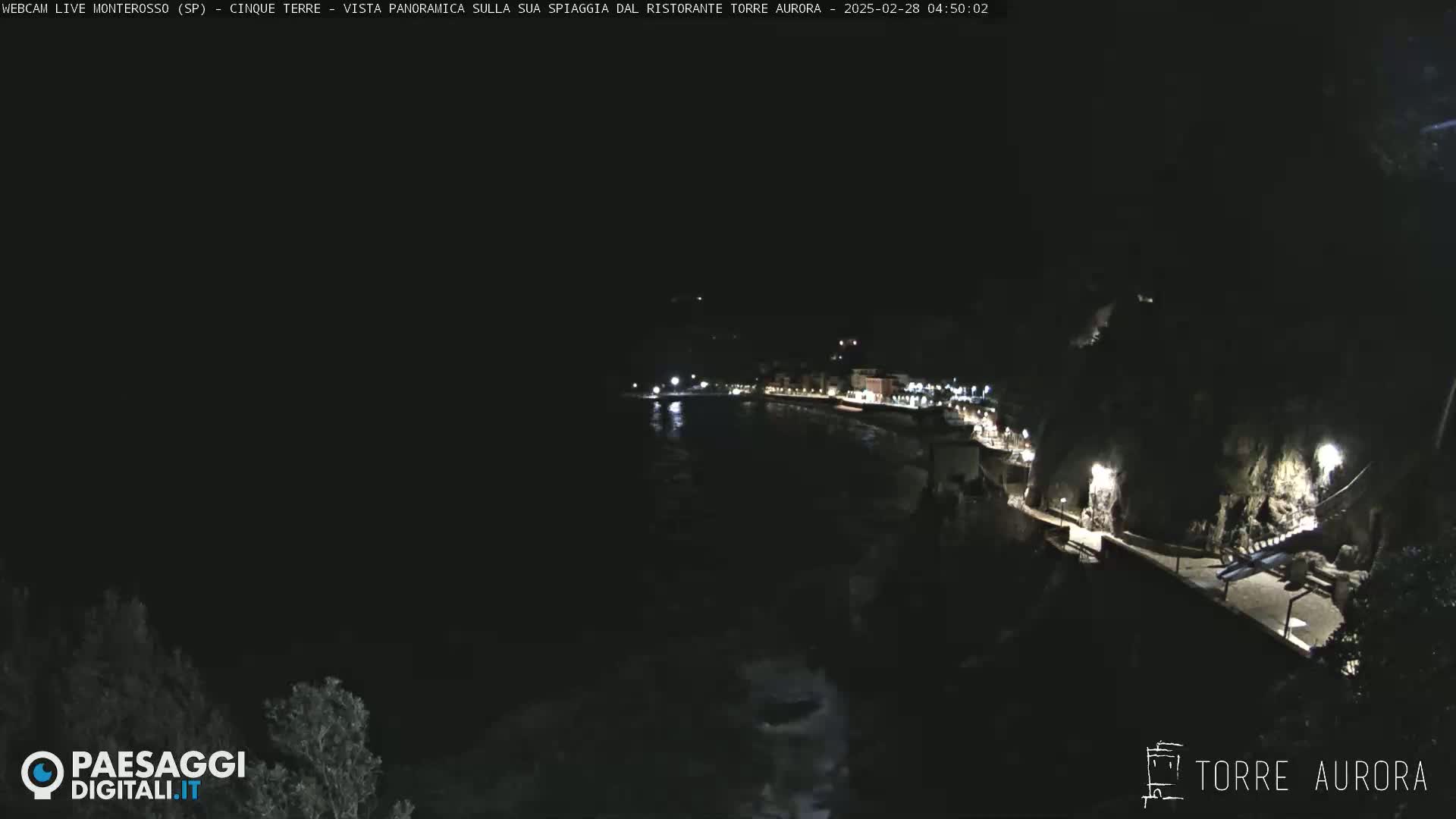A nighttime, panoramic view of a dark, calm body of water next to a dimly lit coastline.
