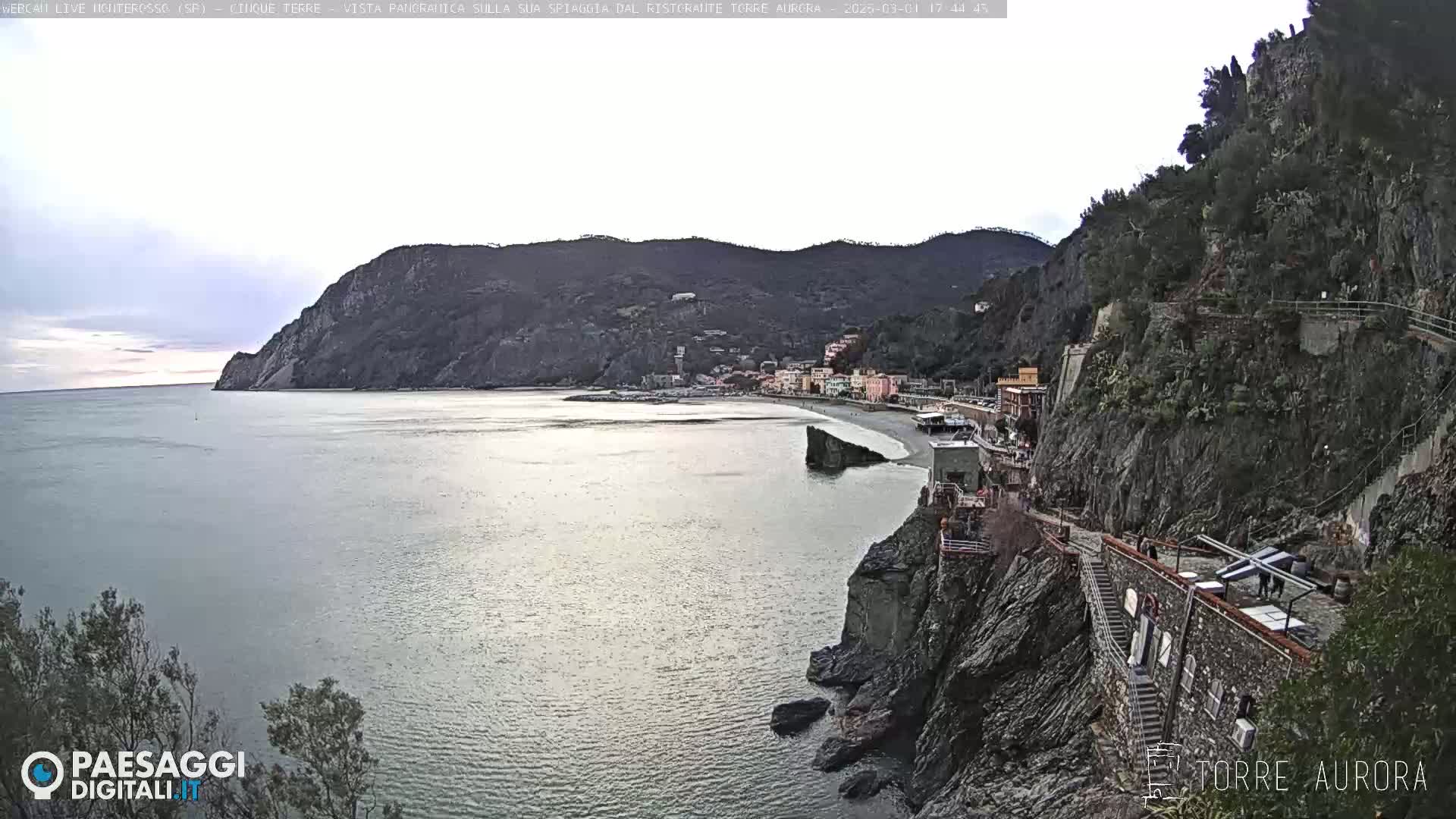 A coastal town nestled between rocky cliffs and a calm sea under a cloudy sky.