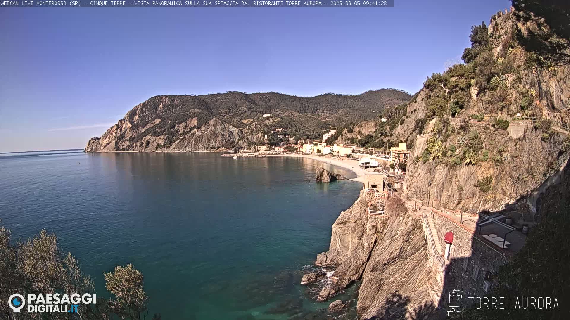 A coastal town nestled between steep cliffs and a clear blue sea under a sunny sky.