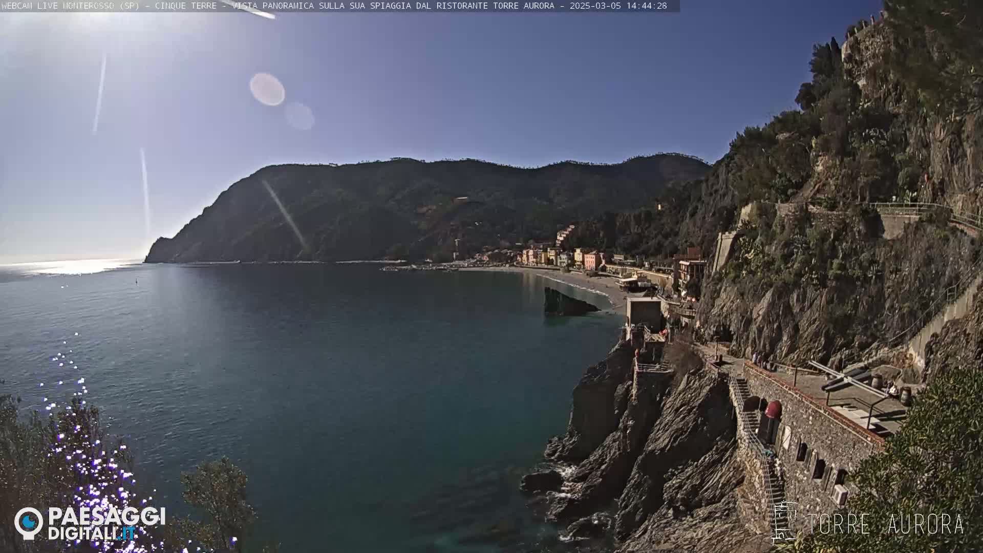 A sunny coastal town nestled between steep cliffs and a calm, dark-blue sea.
