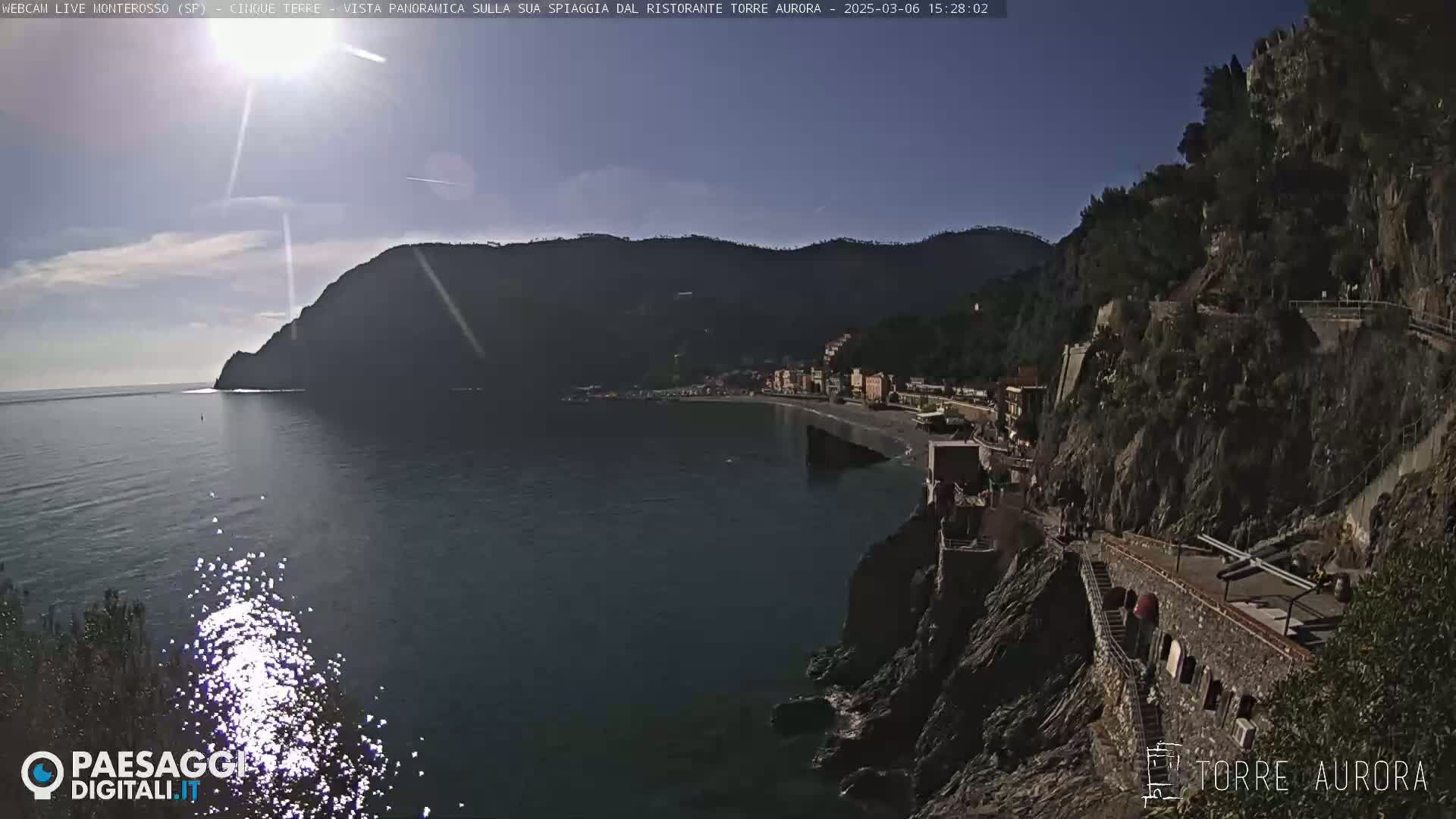 A sunny day shows a coastal town nestled between a rocky cliff and the sea.