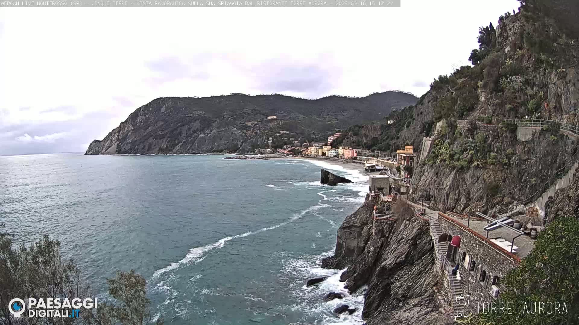 A coastal town nestled between steep cliffs and a blue-green sea under an overcast sky.