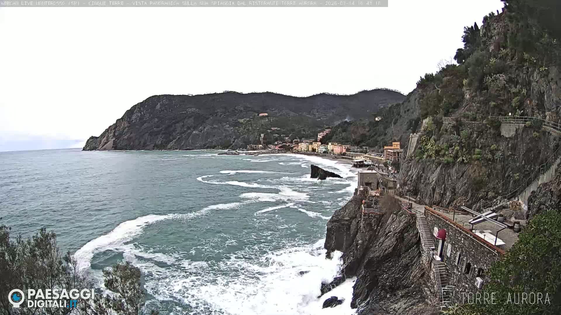 A coastal town nestled between steep cliffs and a turbulent sea under an overcast sky.