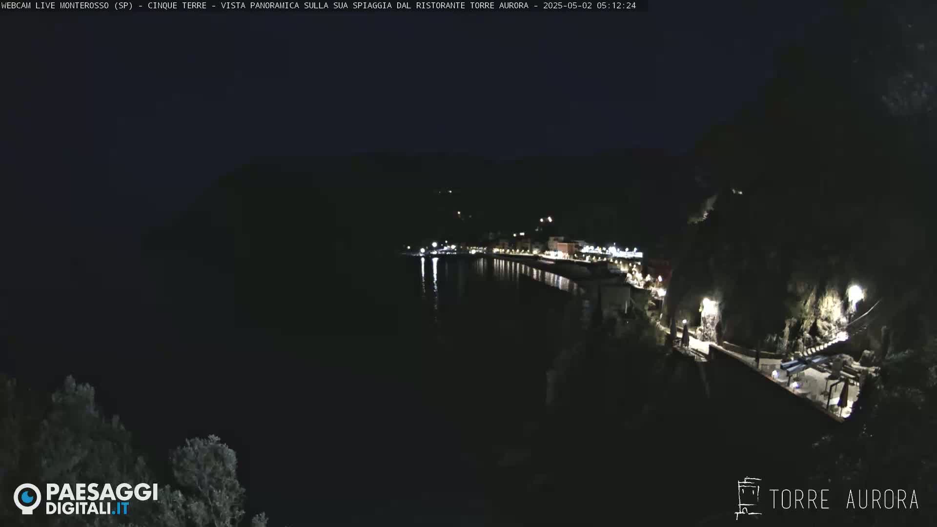 A nighttime, panoramic view of a dark coastline with a few lights visible along the water's edge.