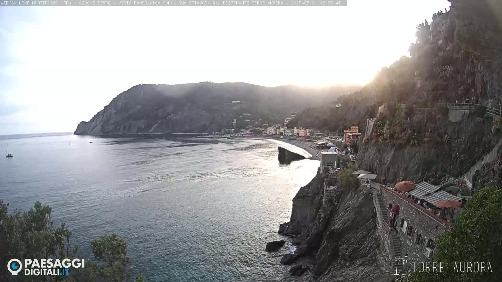 A coastal town nestled between steep cliffs, overlooking a calm sea at sunset.
