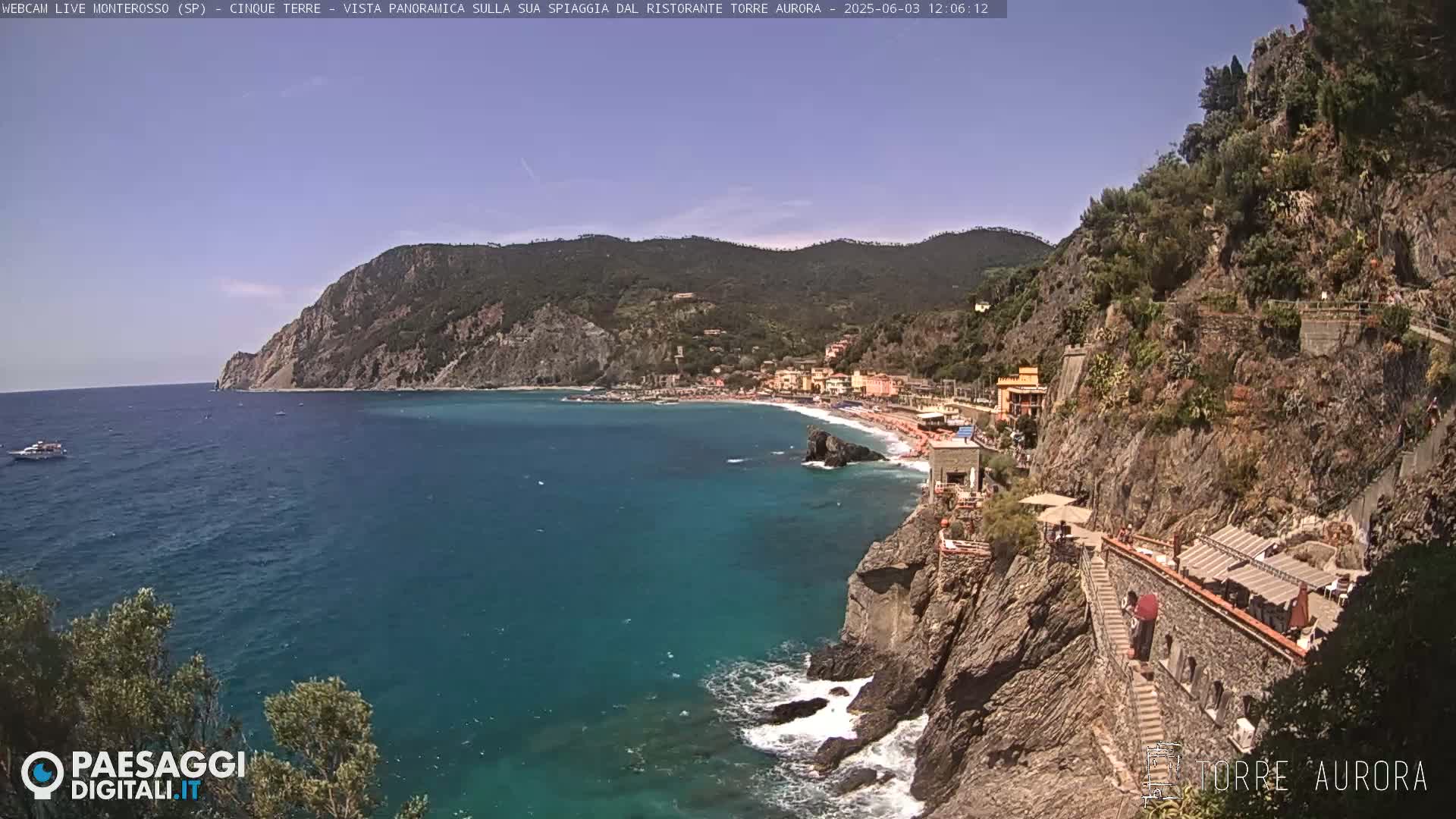 A coastal town nestled between rocky cliffs and a calm turquoise sea under a clear sky.