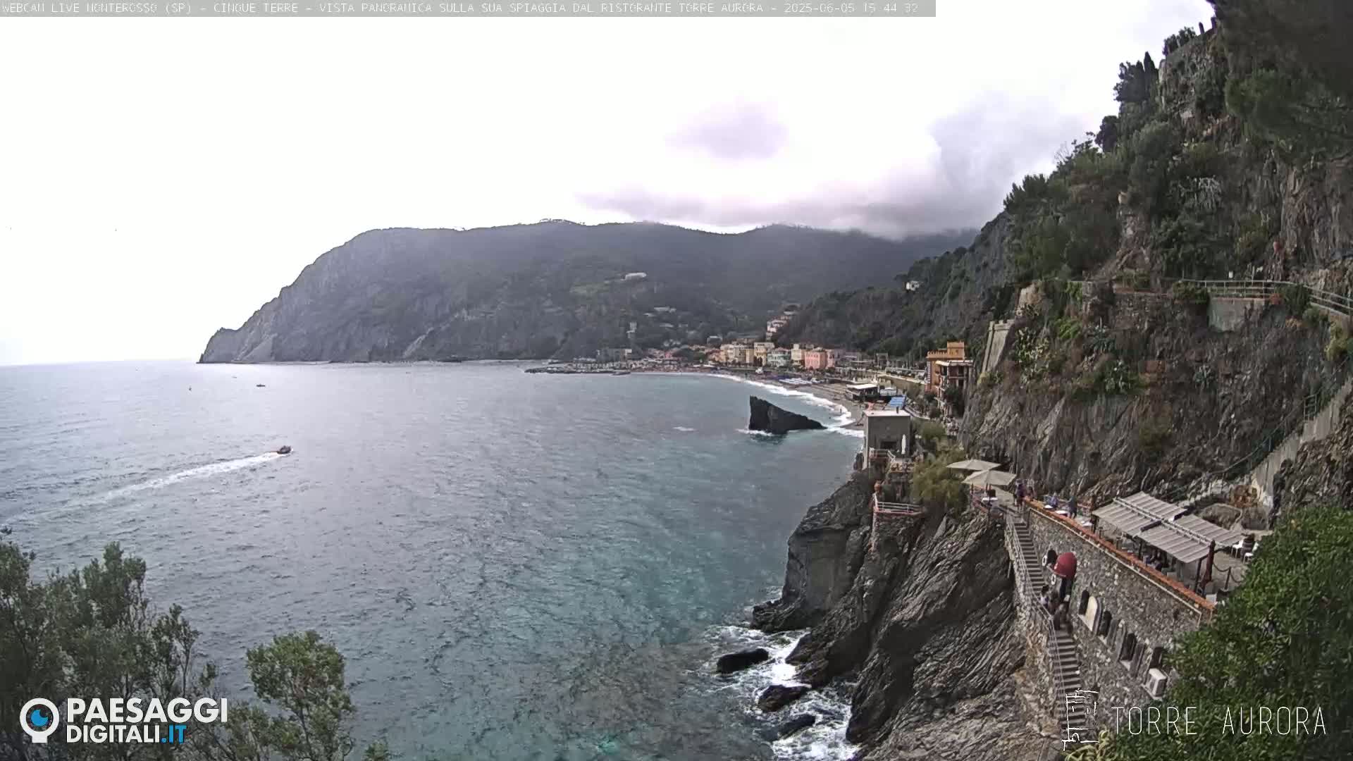 A coastal town nestled between a steep, rocky cliff and a calm sea under an overcast sky.