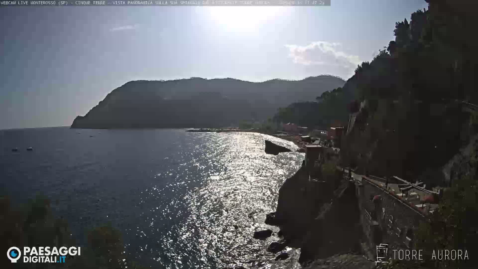 A sunny day overlooking a sparkling ocean next to a rocky shoreline with a town nestled against the hills.