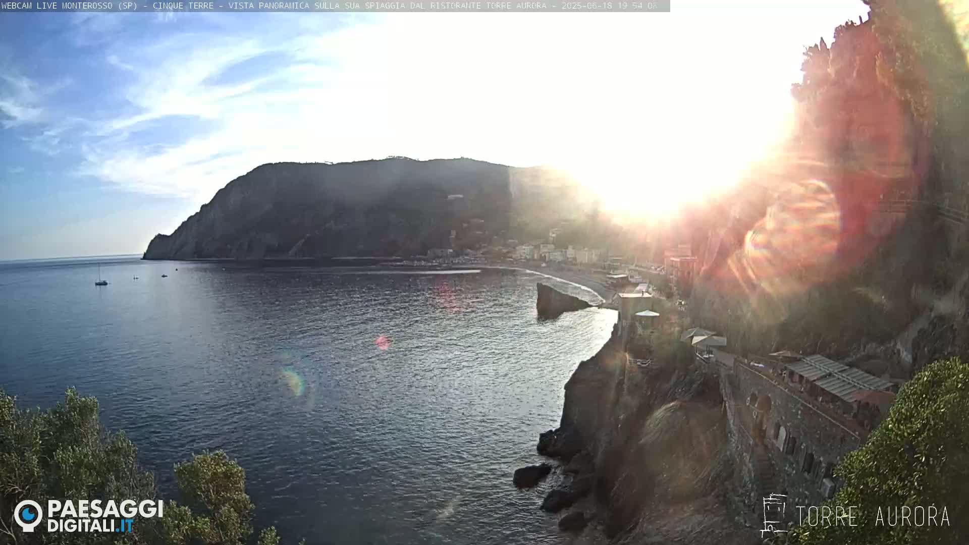 A coastal town nestled between a mountain and the sea, bathed in the golden light of a setting sun.