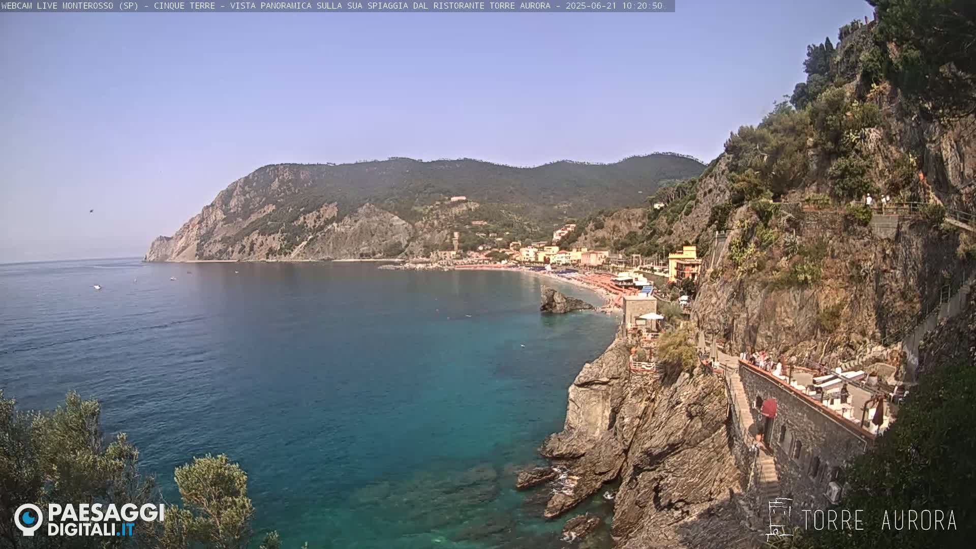A sunny coastal town with a sandy beach nestled between rocky cliffs and a clear blue sea.