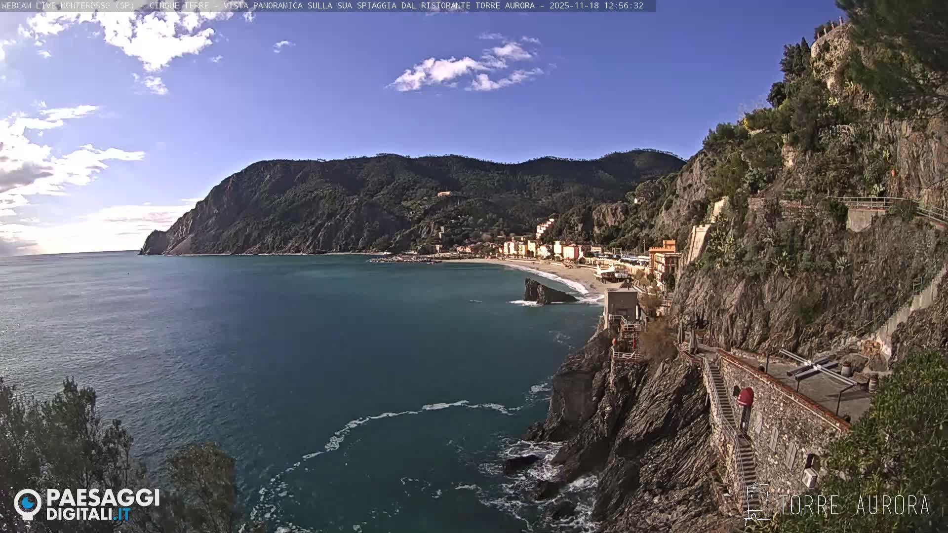 A clear, dark night reveals a panoramic view of a lit-up coastal town with waves crashing against the shore.