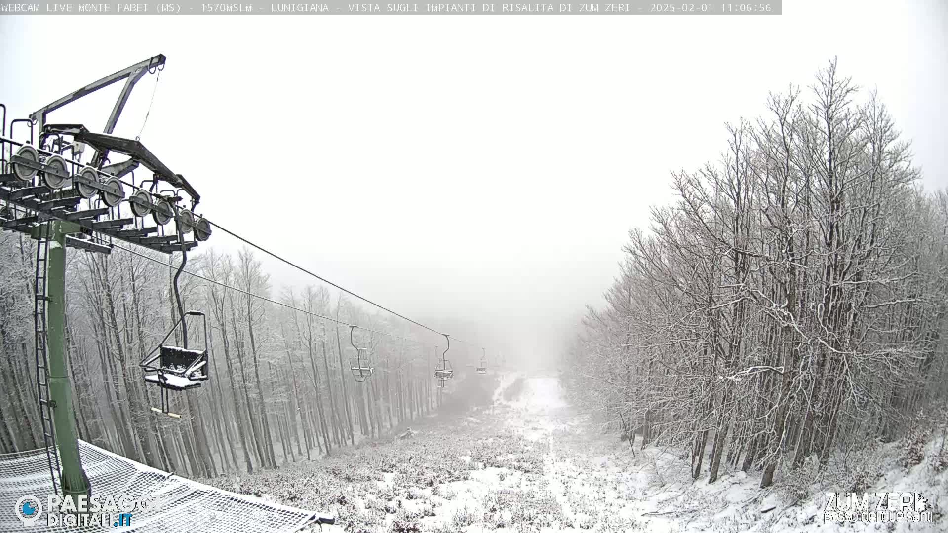 A snow-covered ski lift with several empty chairs ascends a slope through a snow-covered forest in hazy weather.
