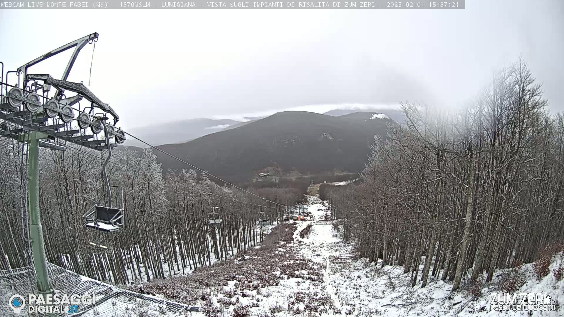 A snow-dusted ski lift ascends a mountainside through a sparsely snow-covered forest under an overcast sky.