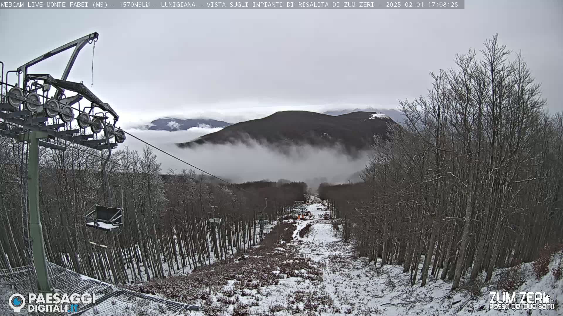 A chairlift ascends a snow-dusted mountainside shrouded in fog, with leafless trees lining the path.