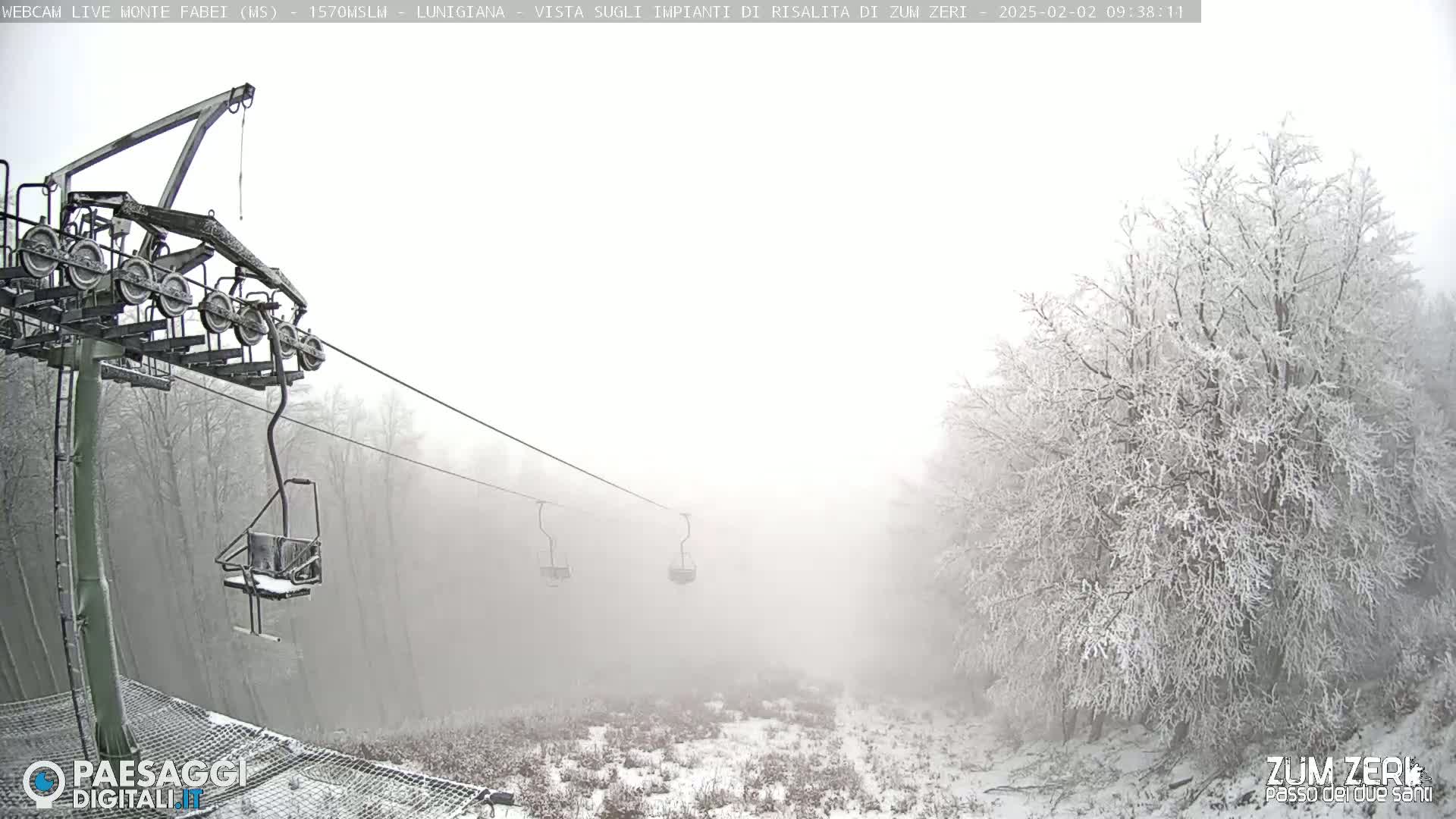 A snow-covered landscape is visible through a thick fog, with a chairlift and its supporting structure in the foreground.