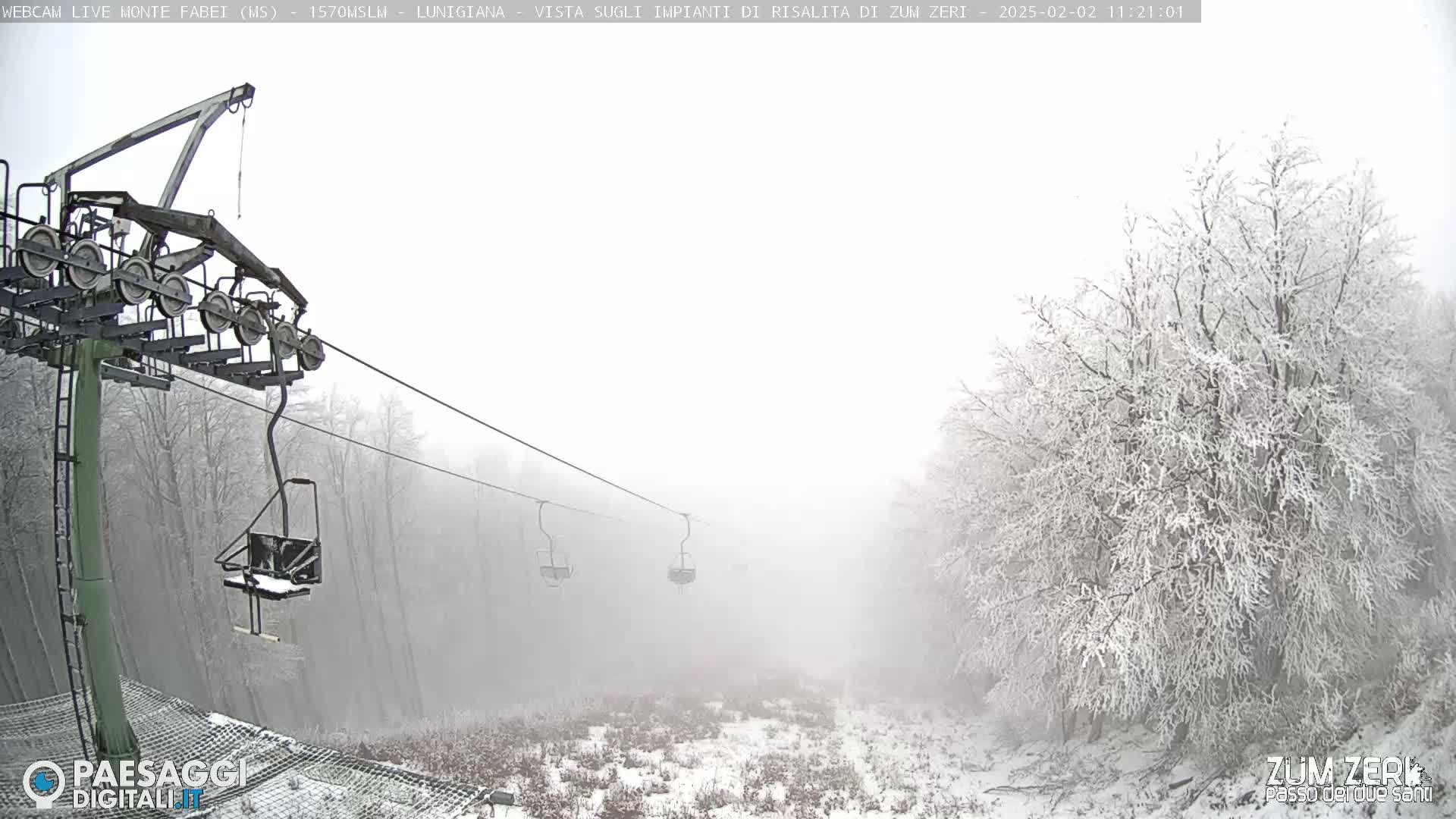 A snow-covered landscape is shrouded in fog, with a chairlift and its supporting structure visible in the foreground.