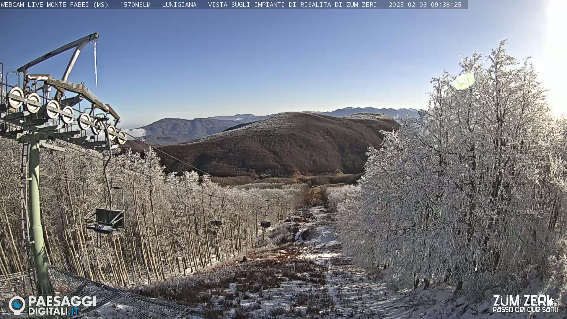 A chairlift ascends a snow-covered mountainside, passing through a forest of frost-covered trees under a clear, sunny sky.