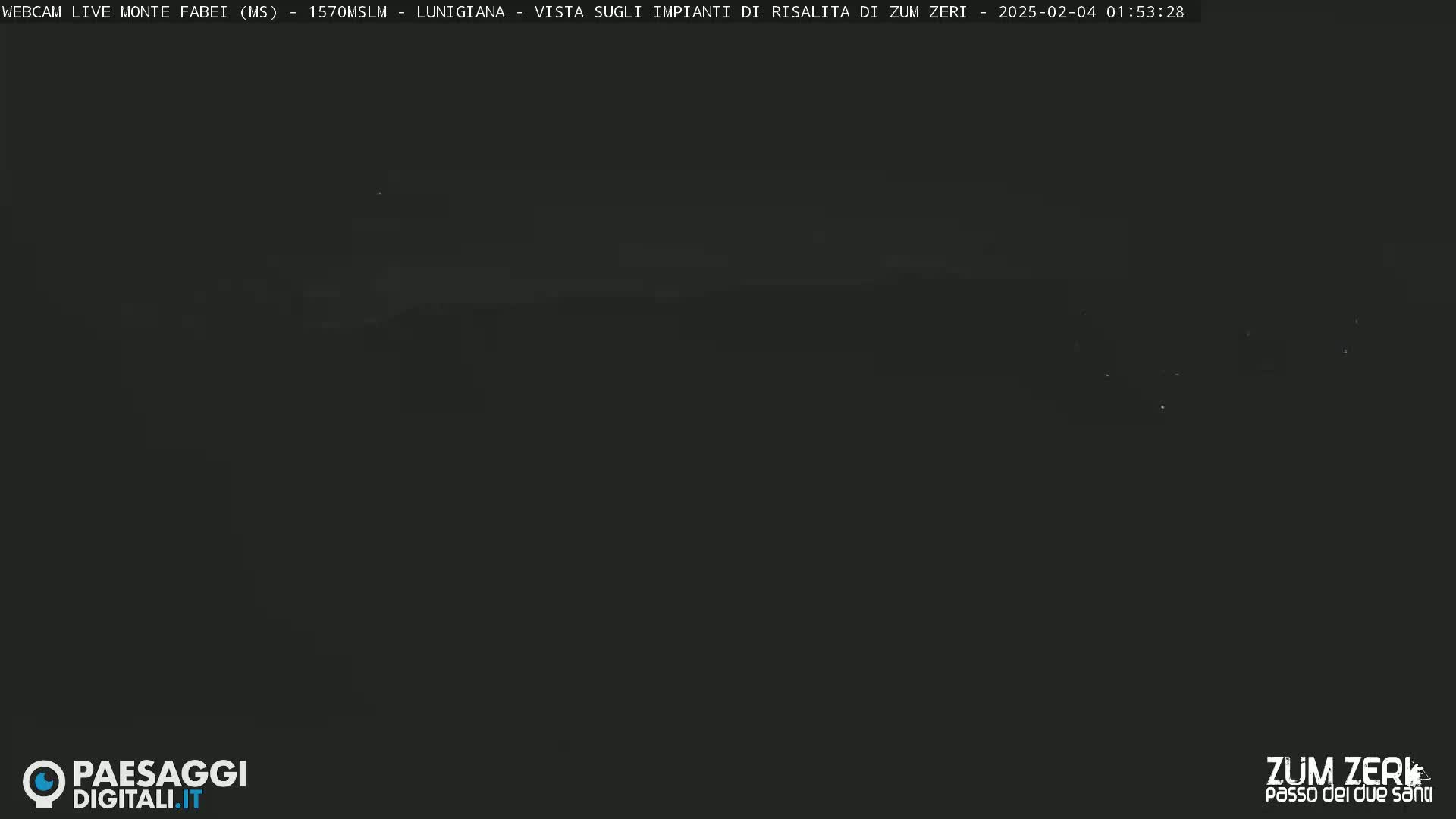 A dark, nighttime view of a mountainous landscape with a few faint lights visible in the distance.