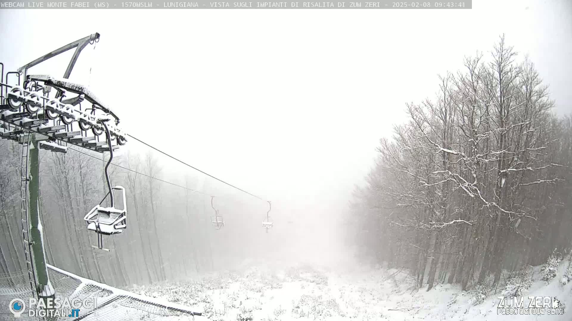 A snow-covered ski lift chair and cables are visible in a snowy, foggy landscape with snow-covered trees.