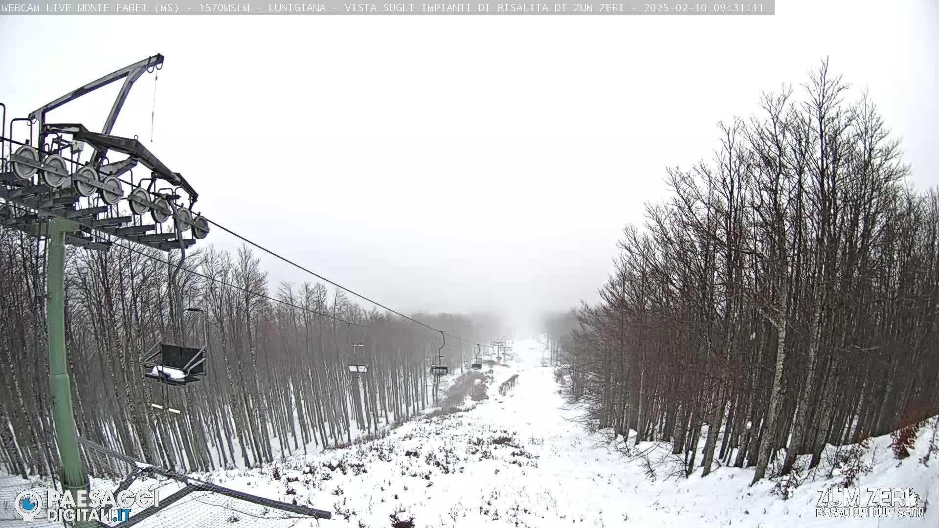 A snow-covered ski slope with a chairlift and bare trees under an overcast sky.