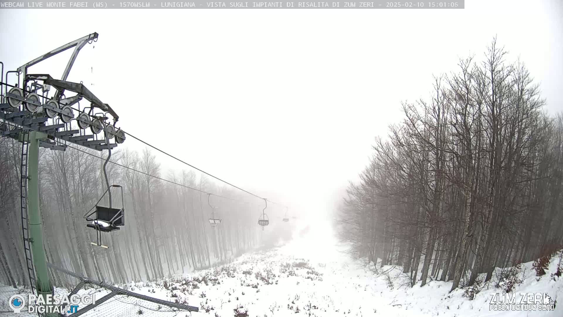 A snow-covered ski lift ascends through a foggy forest.