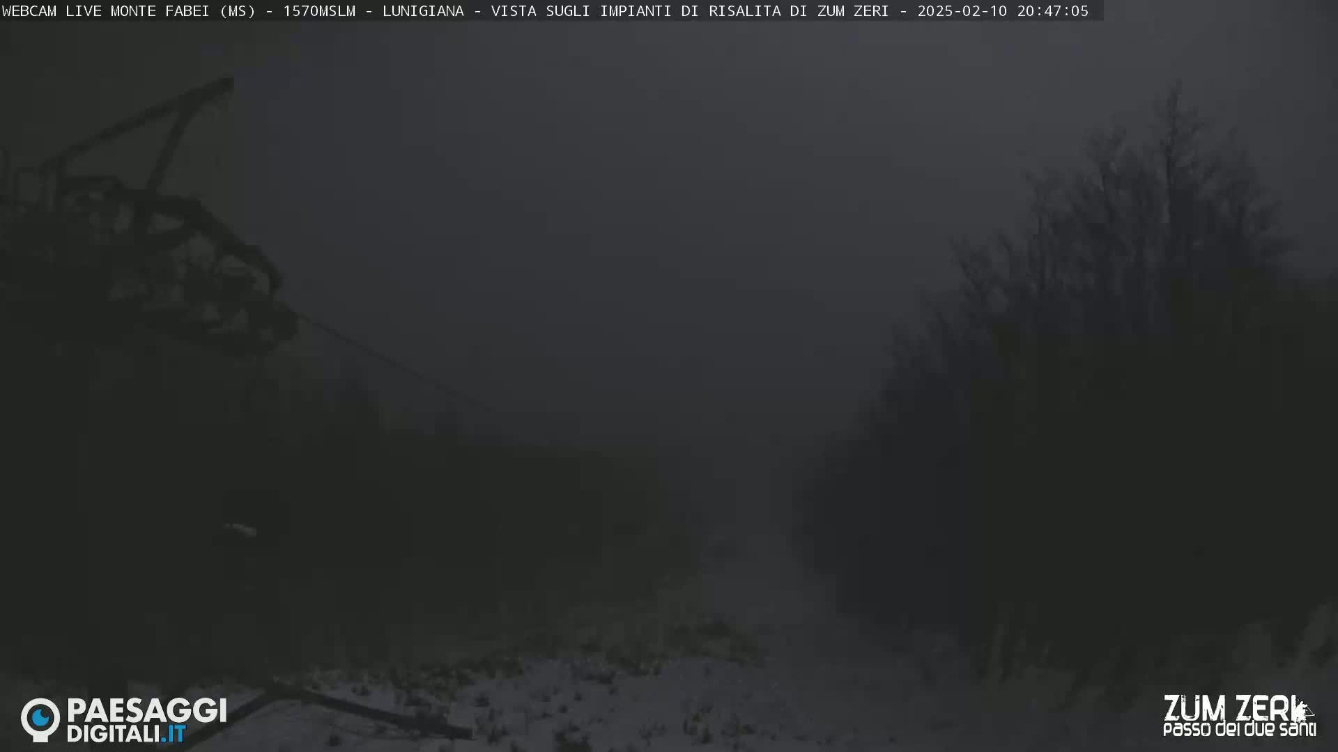 A dark, foggy scene shows a chairlift and some snow-covered ground.