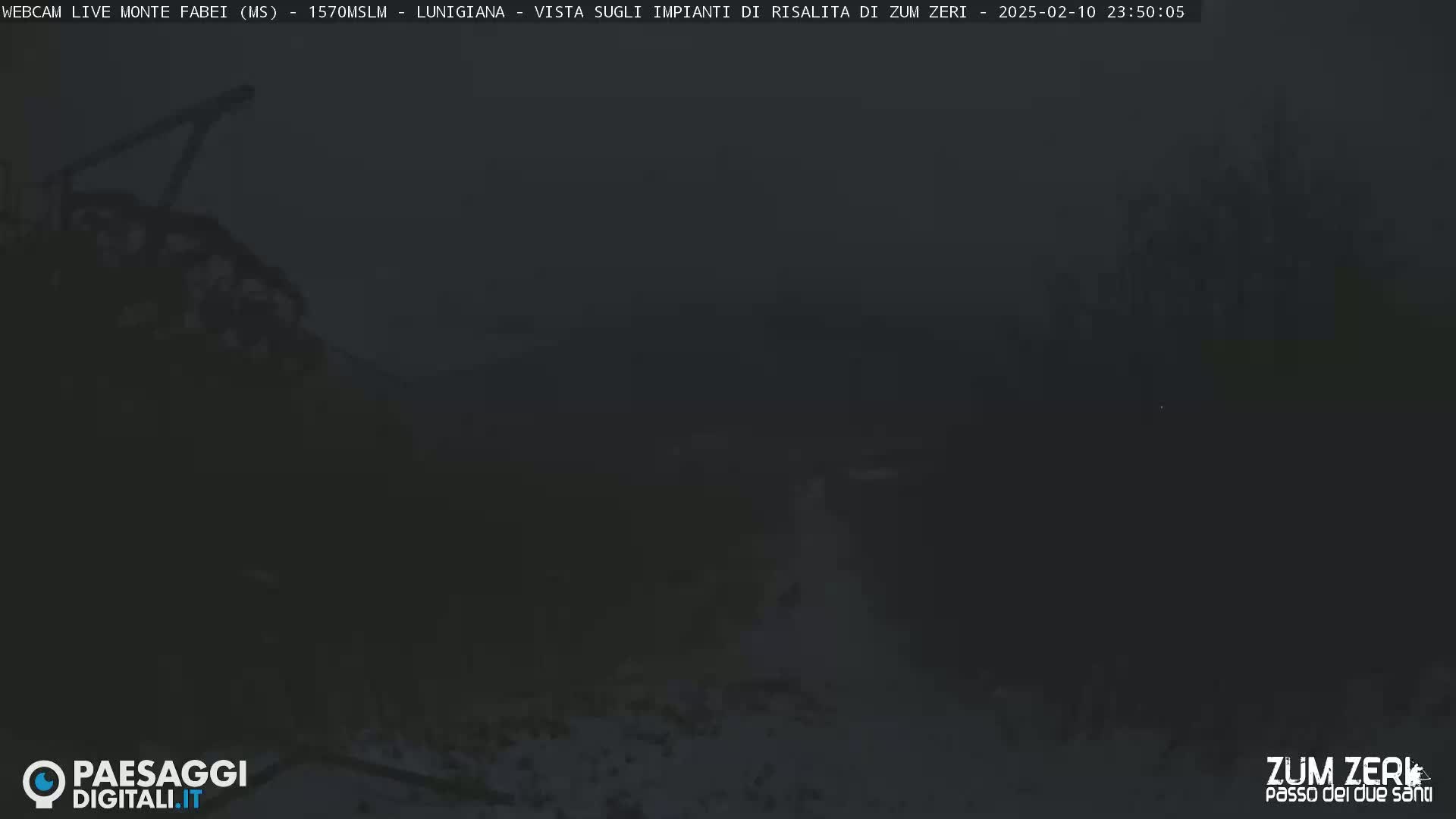A dark, foggy nighttime scene shows indistinct shapes of what appears to be mountainous terrain and possibly some structures.